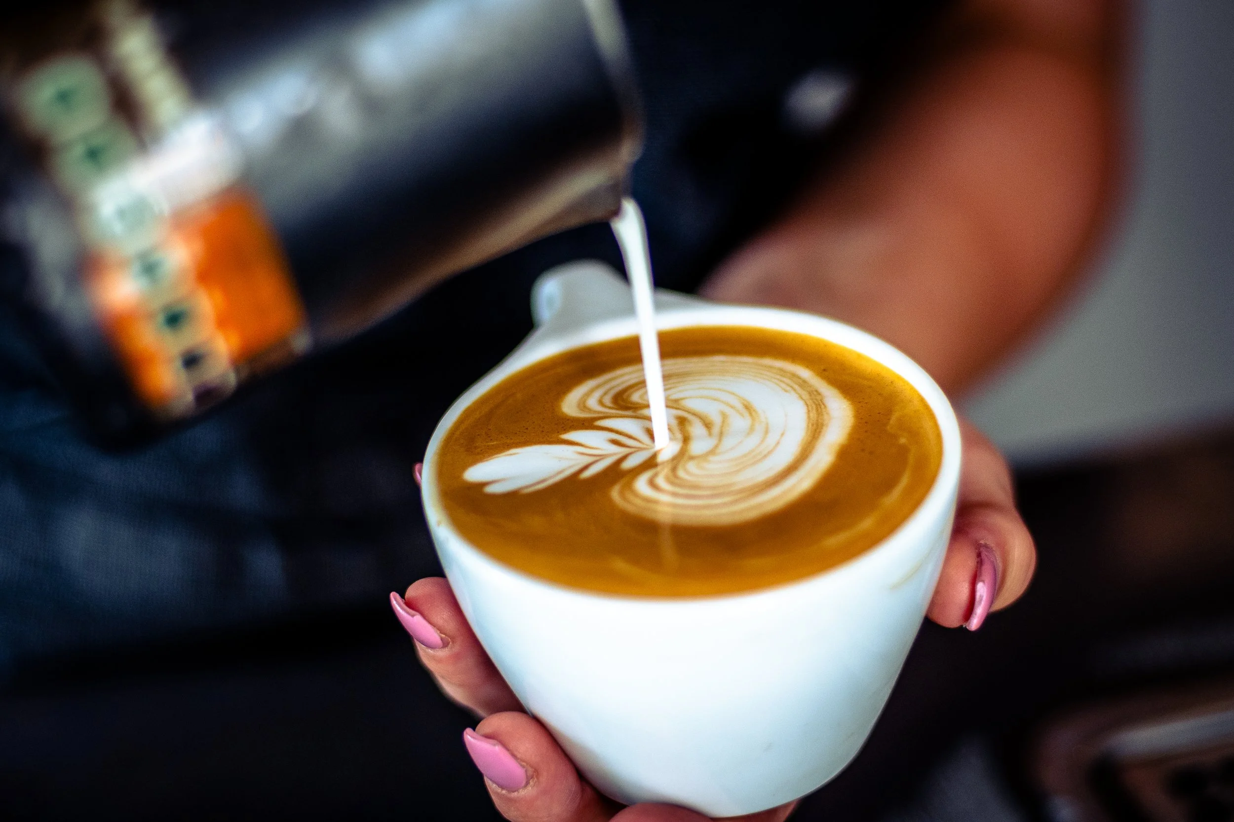 Barista pouring milk into a cup of coffee to create latte art with a leaf design.