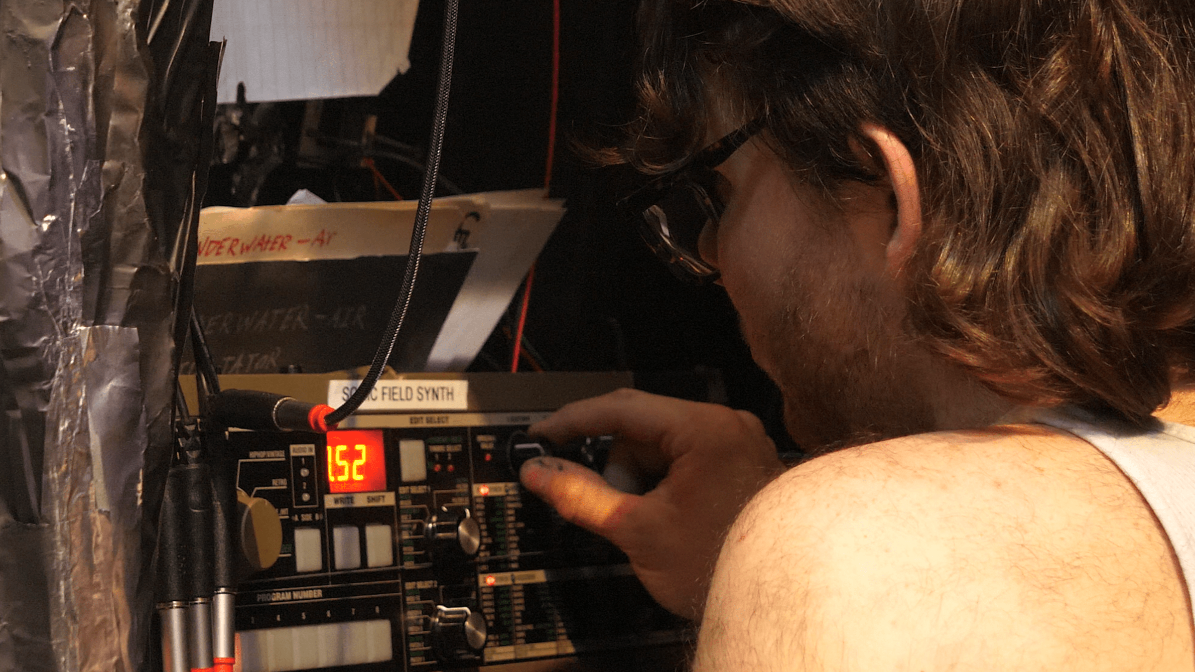 Person adjusting knobs on audio equipment with cables attached.
