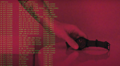 A red-tinted image showing a hand holding a wristwatch. In the background, there is a screen displaying network connection data, including IP addresses, port numbers, and connection statuses such as "ESTABLISHED" and "CLOSE_WAIT."