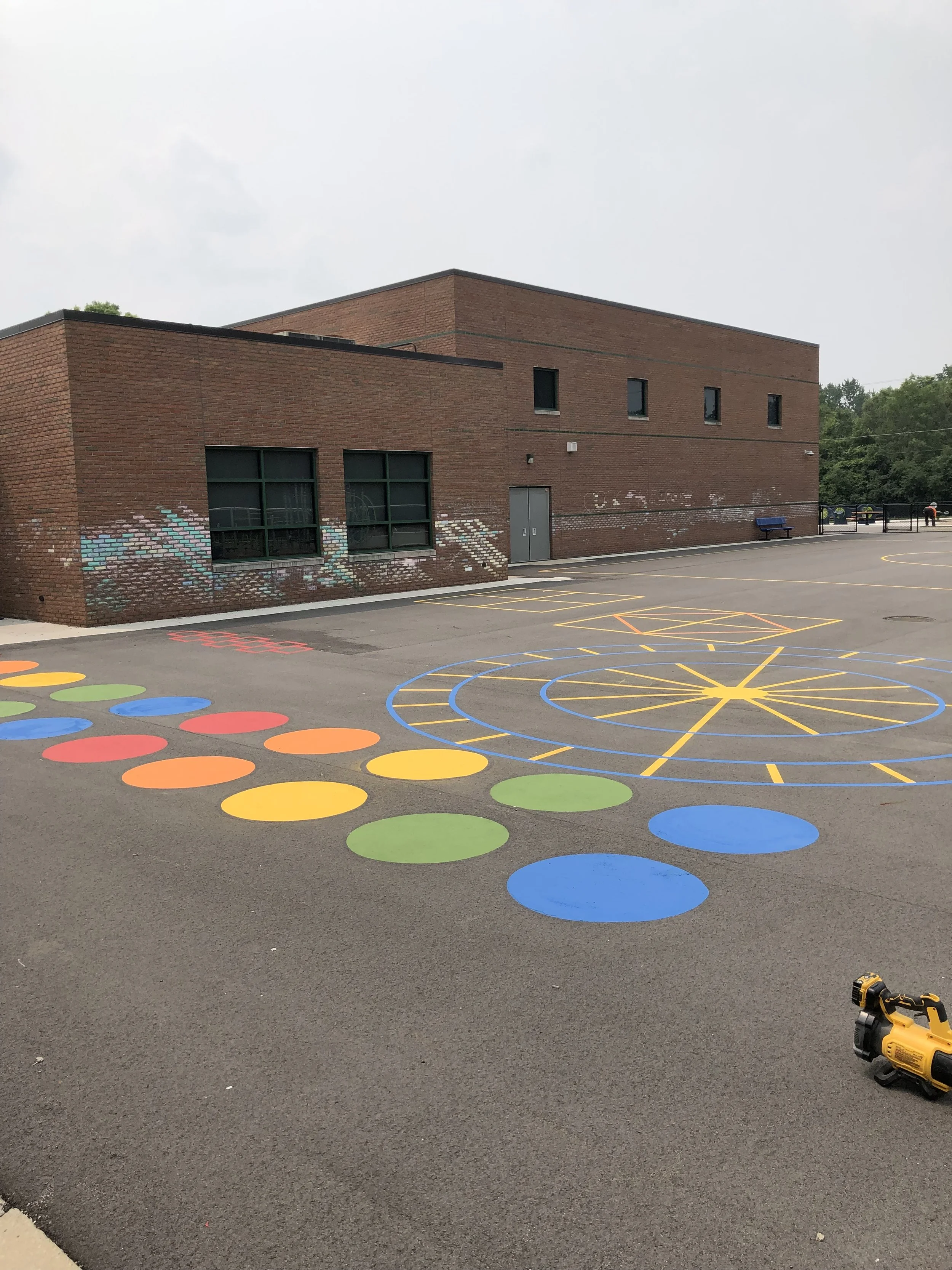 Colorful hopscotch game painted on school playground with a brick school building in the background.