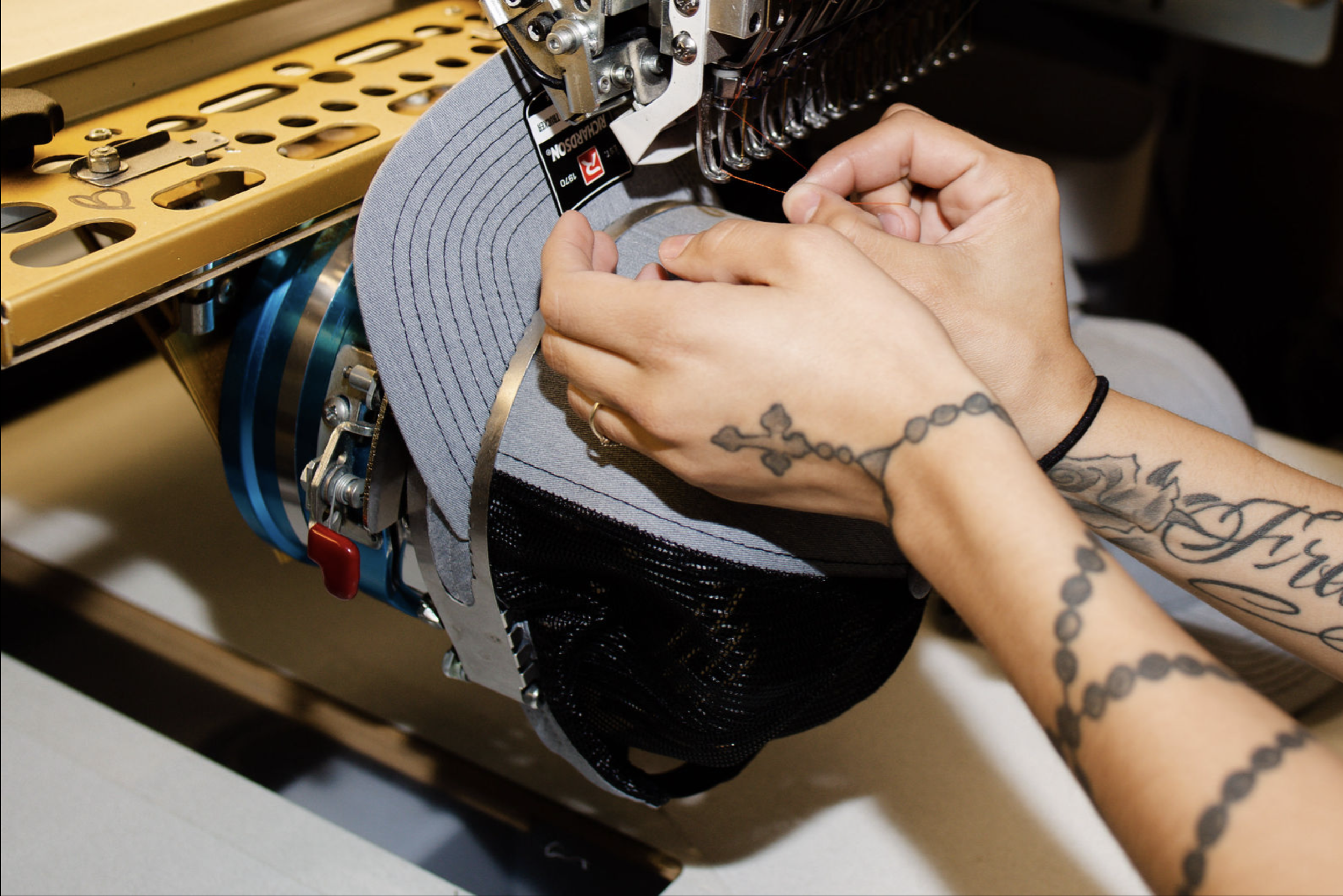 A person is setting up a grey and black cap on an embroidery machine for stitching.