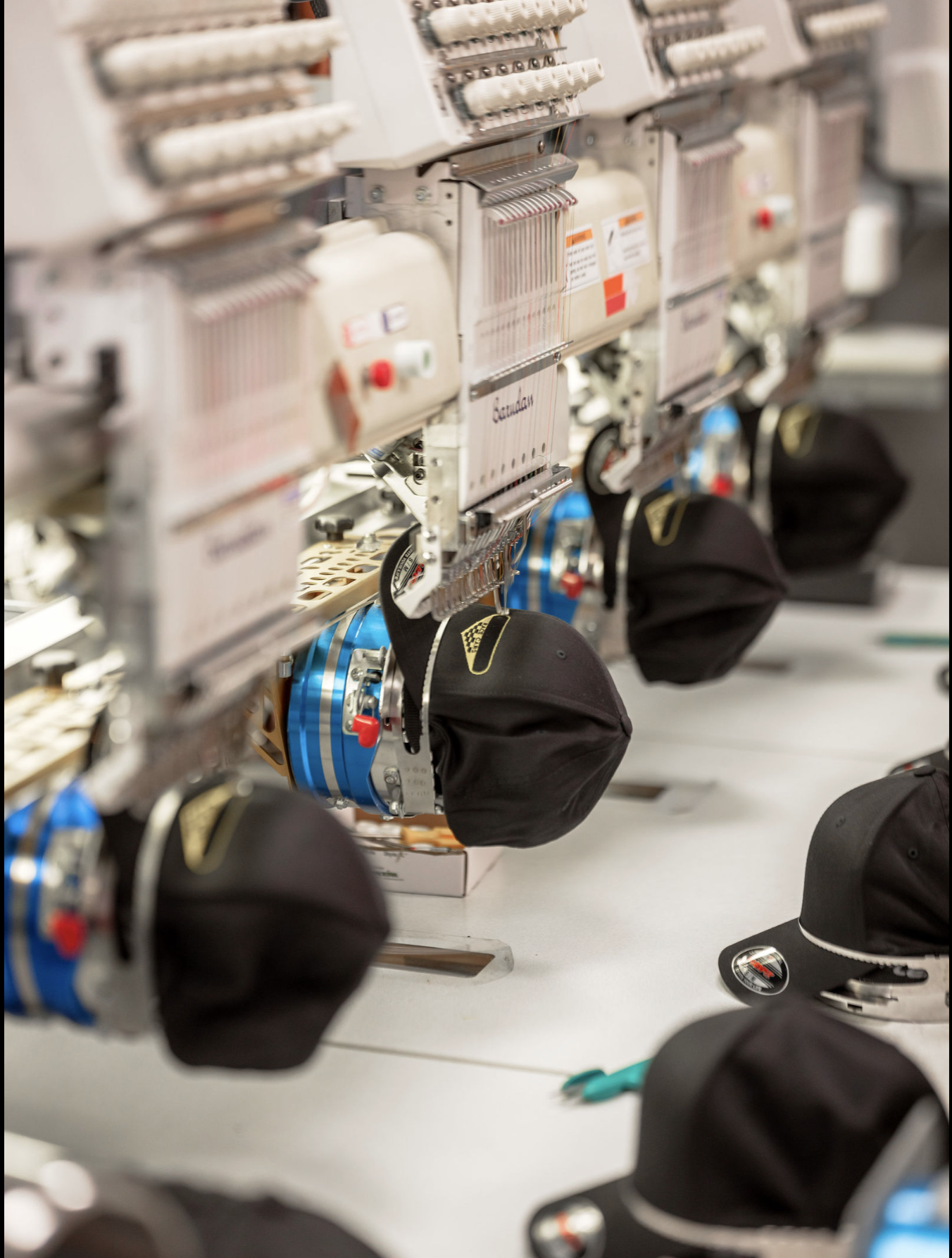 Multiple black caps are being embroidered simultaneously on a row of automated embroidery machines.