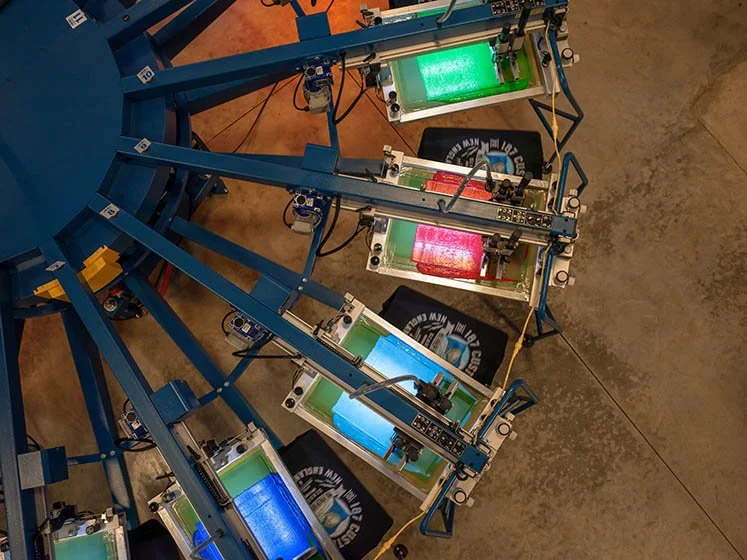 A large machine with various colored shirts hanging on hooks, ready for printing and customization.