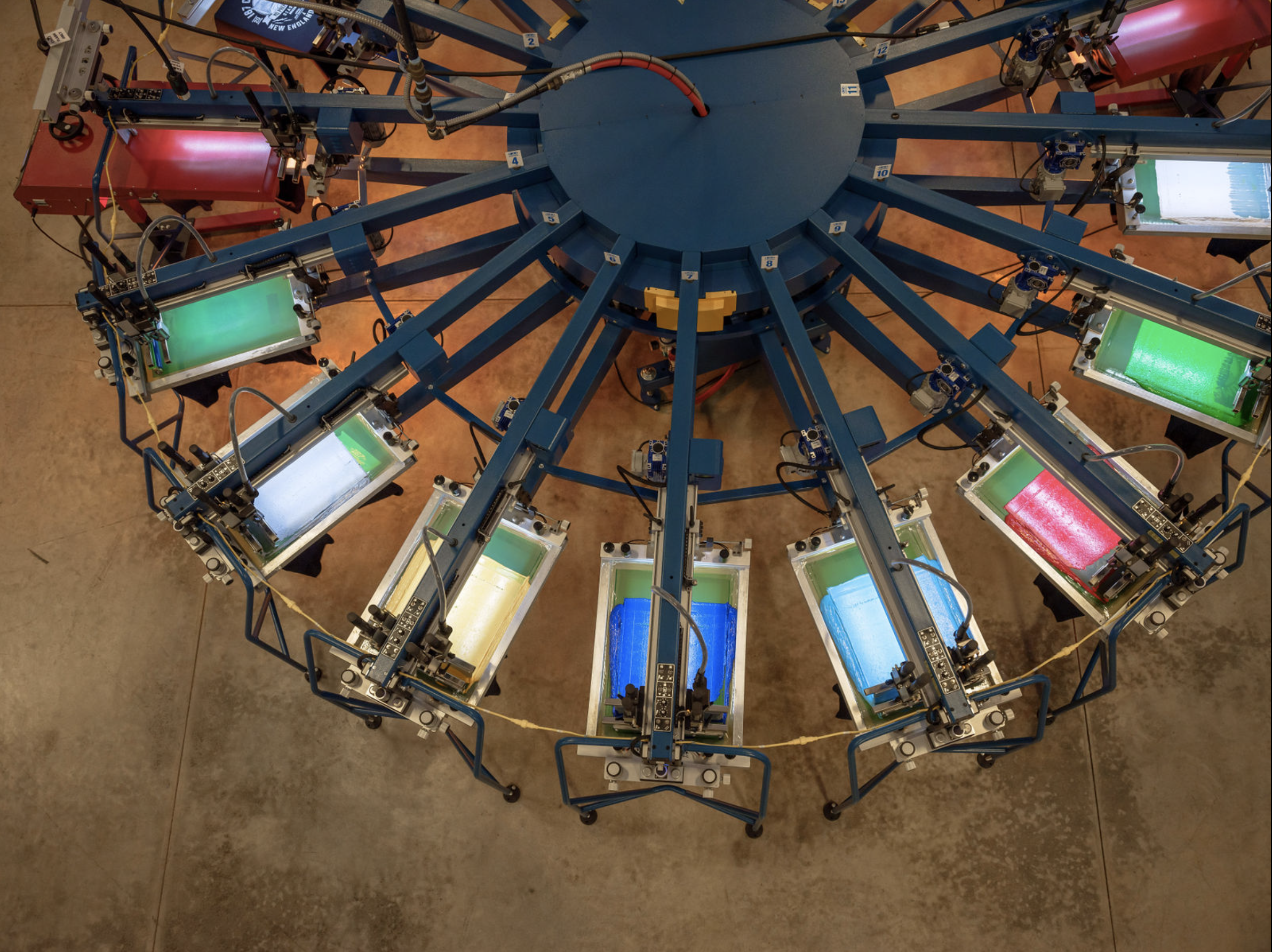 A large circular automated screen printing machine holds multiple screens with different colored inks for printing multicolor designs on garments.