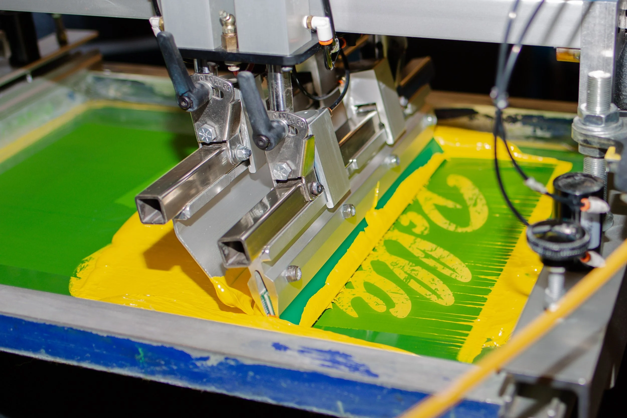 Silkscreen machine producing yellow paint onto green fabric.