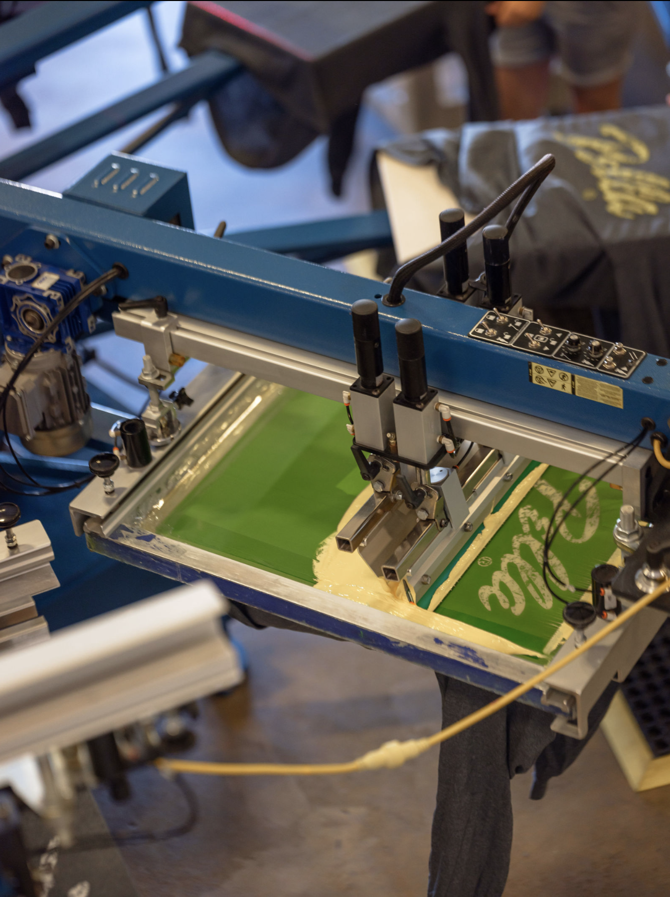 A screen printing machine is applying yellow ink onto a dark t-shirt through a green stencil.