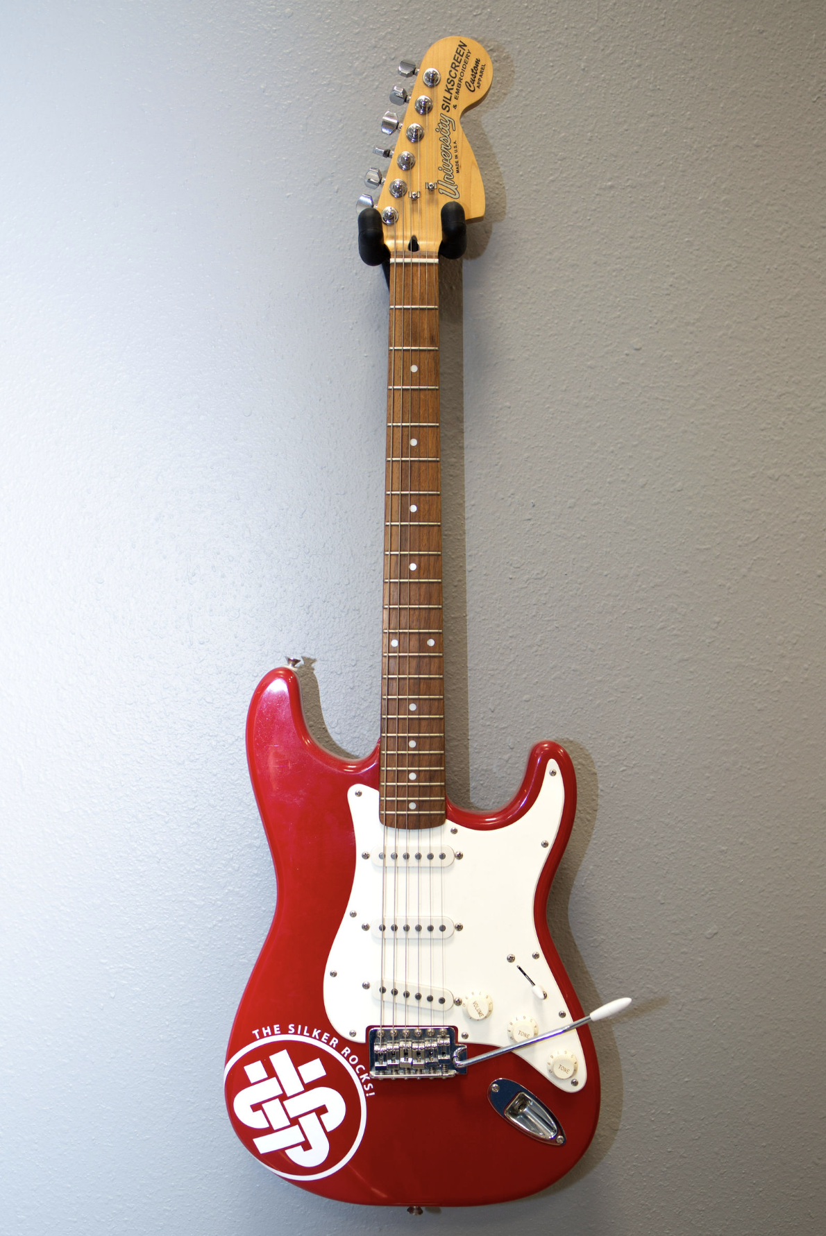 Red electric guitar featuring a custom printed logo displayed on a wall.