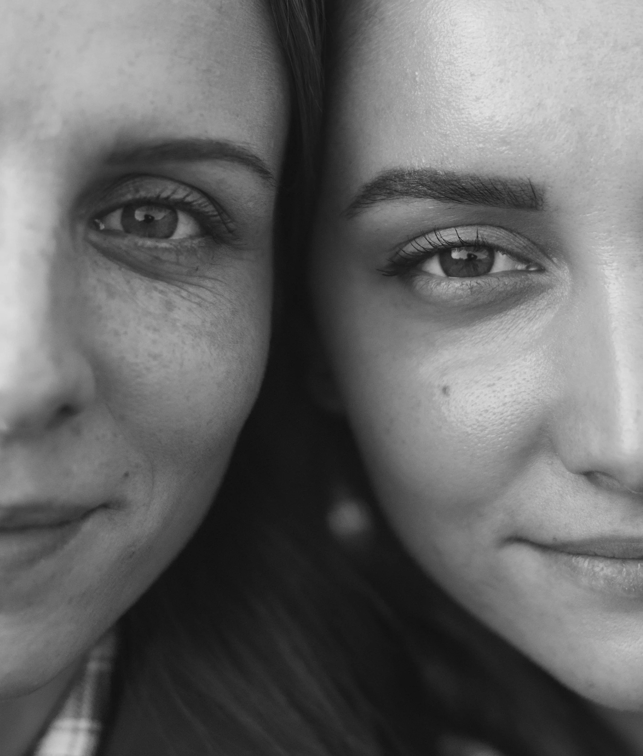 Close-up black and white portrait of two women, showing partial faces with focus on their eyes and smiles.