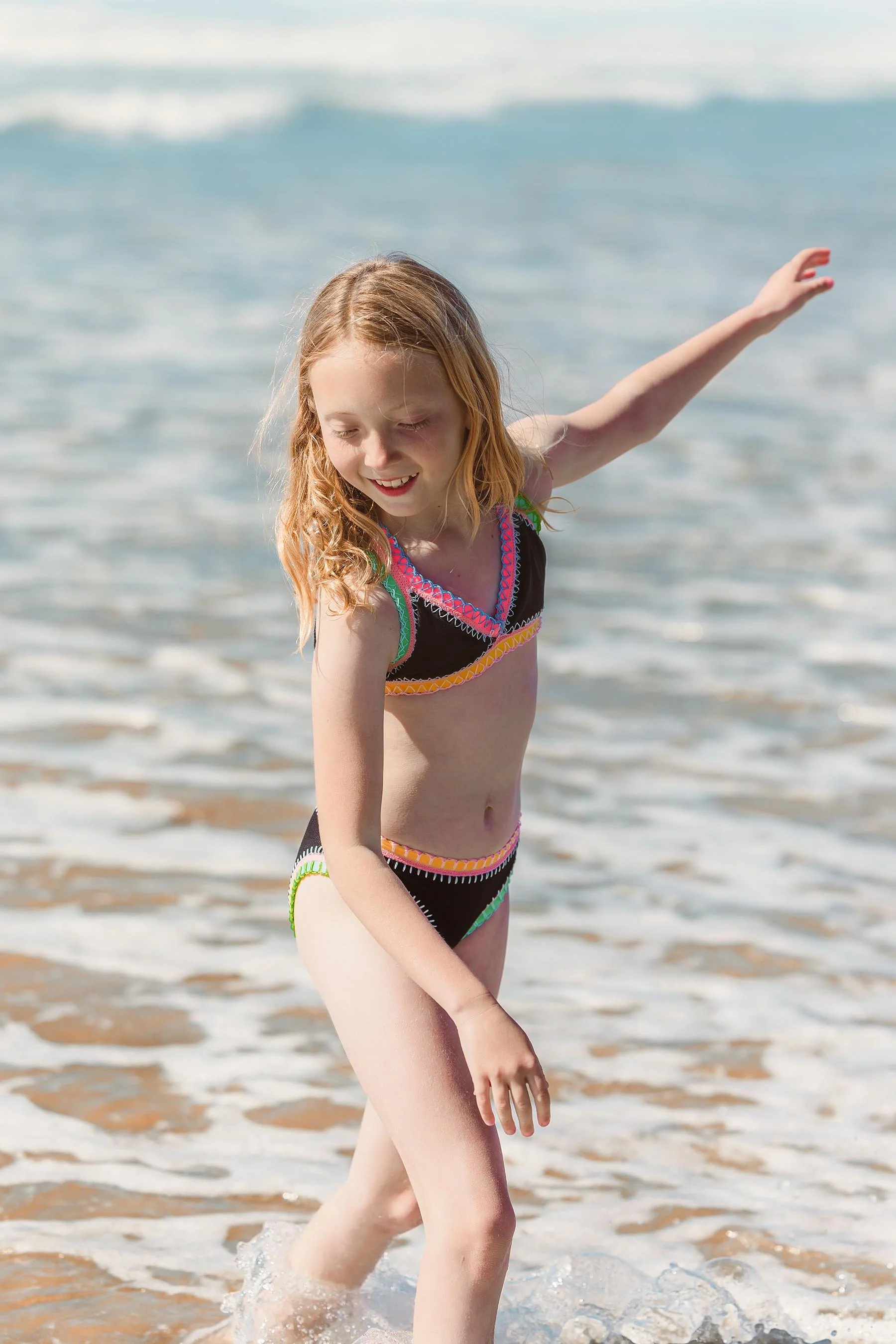 Young girl in a colorful bikini playing in the ocean waves at the beach.