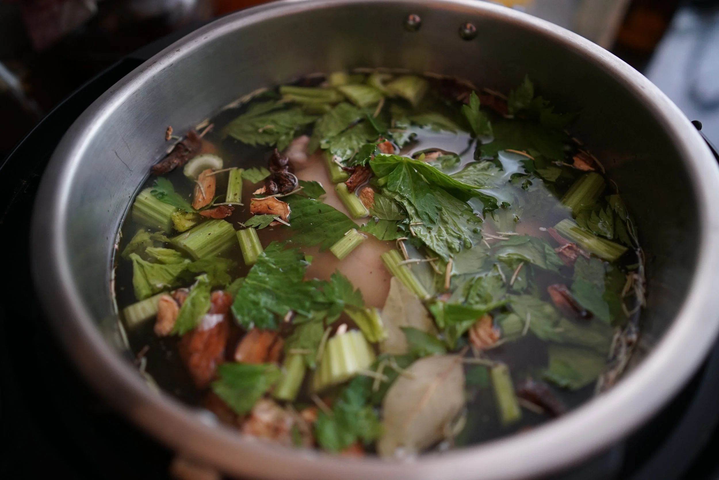 Here's what it looks like when everything has been added to the pot of soup. You can see a steel pot, nearly full of liquid that contains celery chunks, some herbs and the chicken just below the surface.