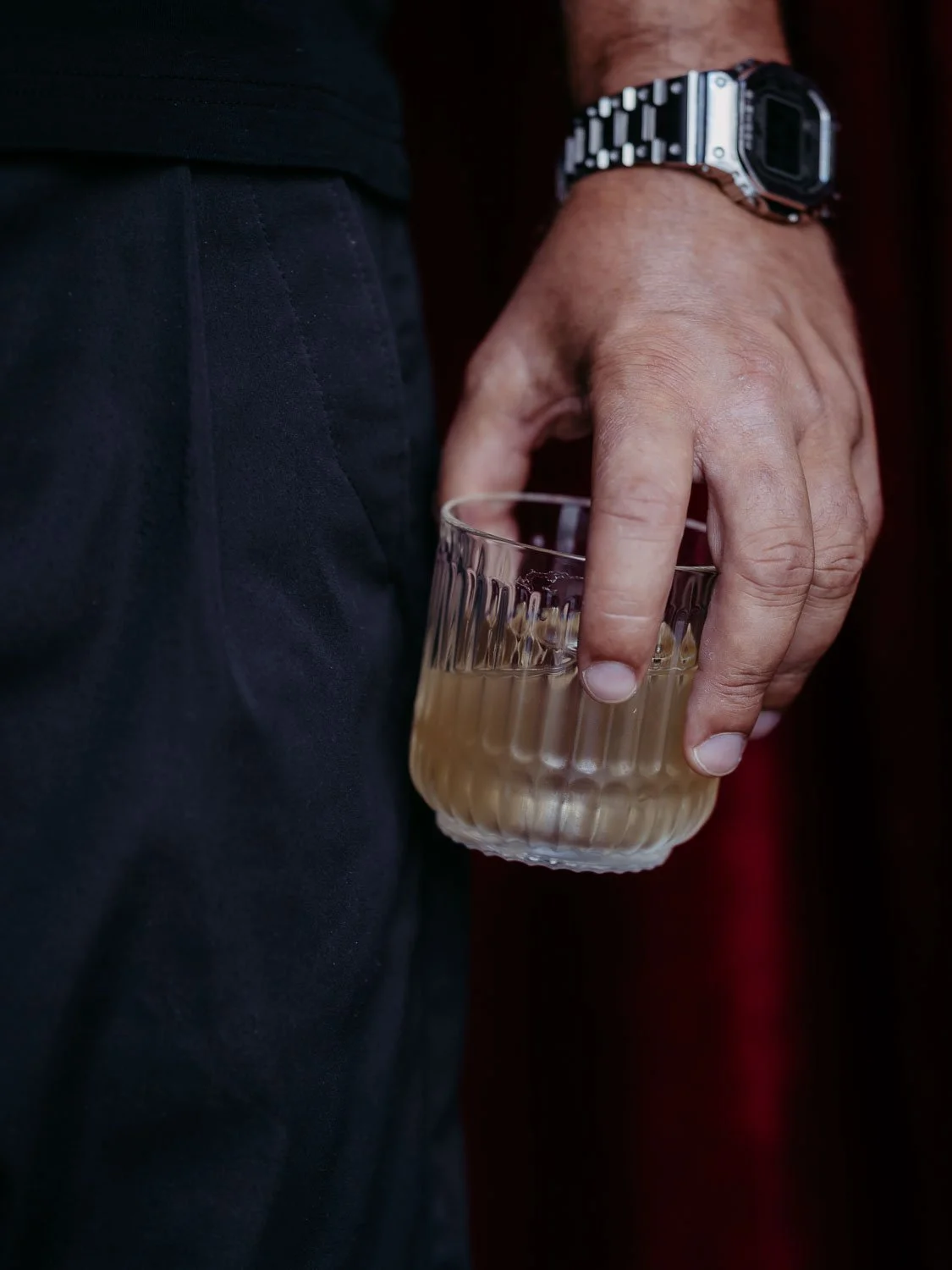 Close-up Foto einer Hand, die einen Cocktail vor einem roten Vorhang hält