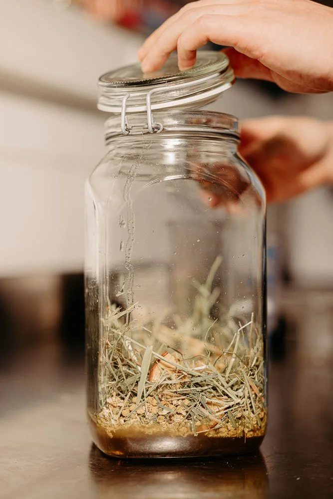 Ein Einmachglas mit Botanicals wie Heu und Apfelund eine Hand schließt das Einwecklglas.