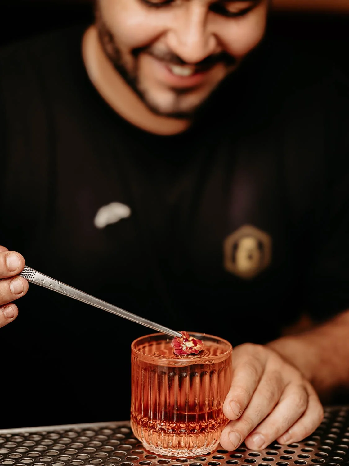 Ein Barkeeper garniert einen roten Cocktail mit einer Blüte
