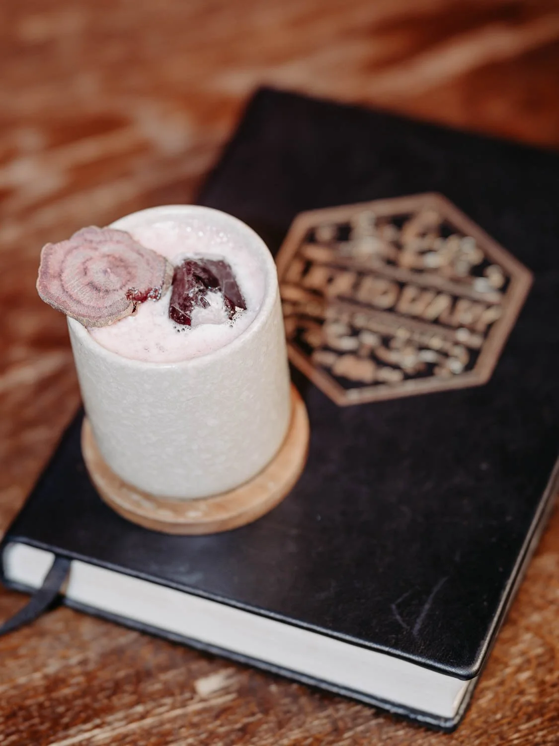Ein Cocktail in einer Keramikgefäß steht auf einem dicken Tagebuch, garniert mit einem Rote Beete Chip