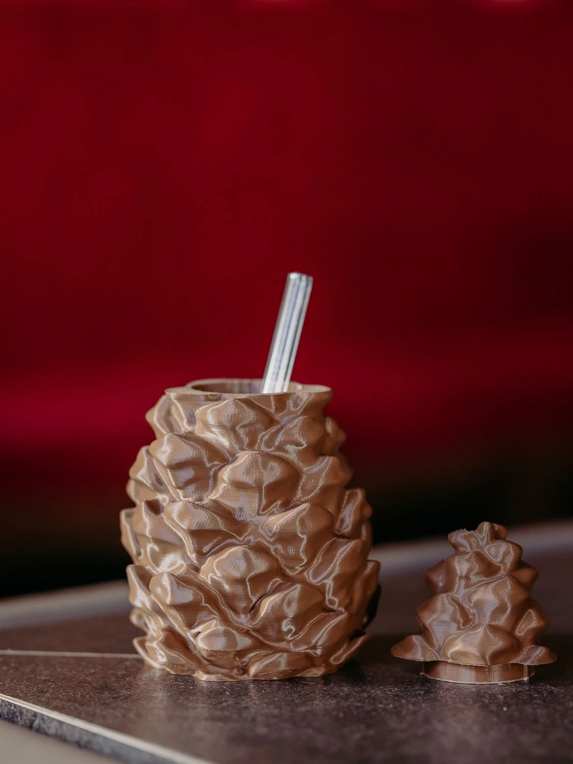 Ein ungewöhnlicher Becher aus silbernem, gewelltem Material mit einem Strohhalm, der auf einer Oberfläche vor rote Hintergrund steht.
