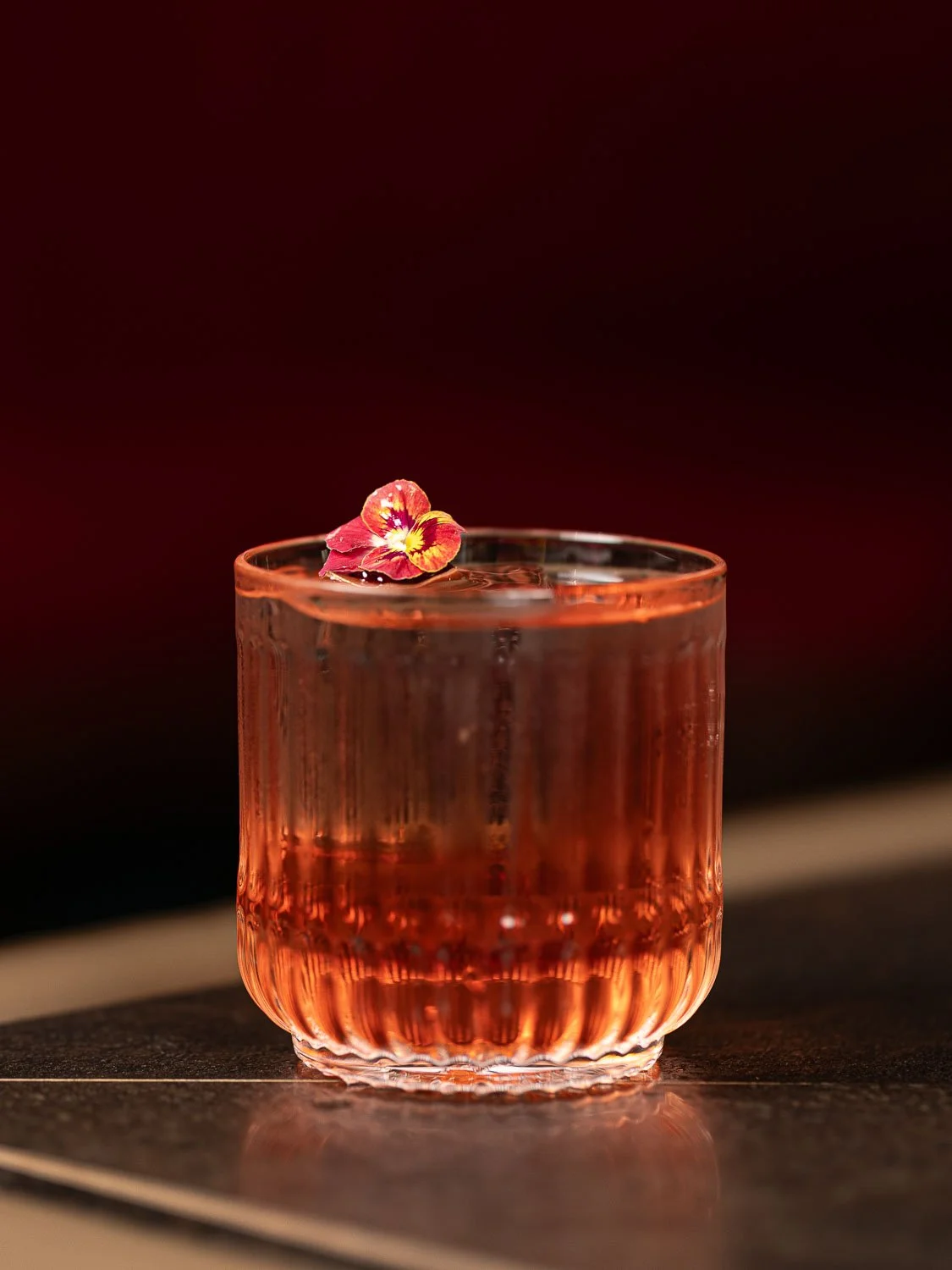 Roter Cocktail in einem Riedel Cocktailglas garniert mit einer roten Blüte
