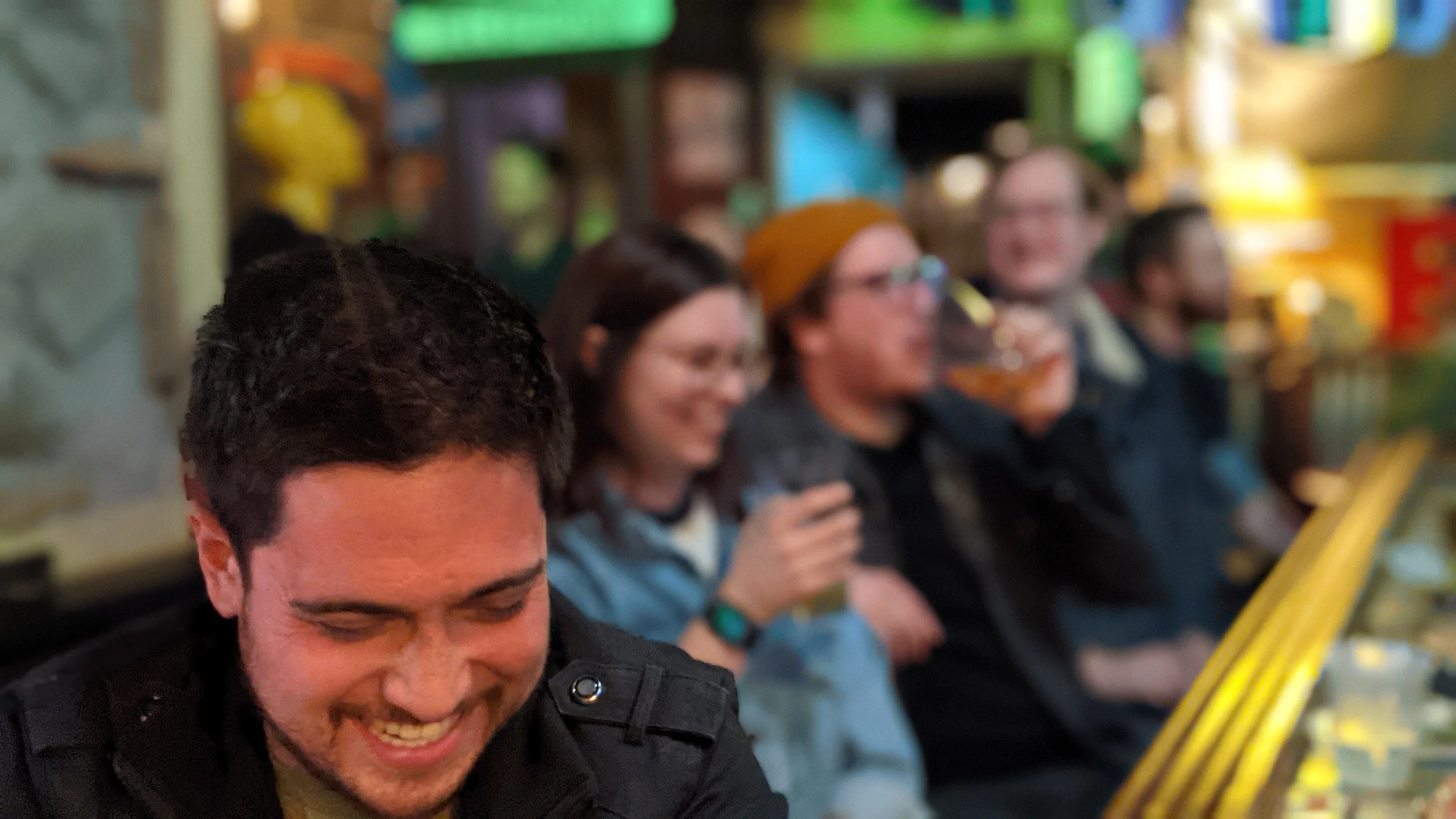Group of people sitting together, smiling and enjoying themselves in a colorful indoor setting.