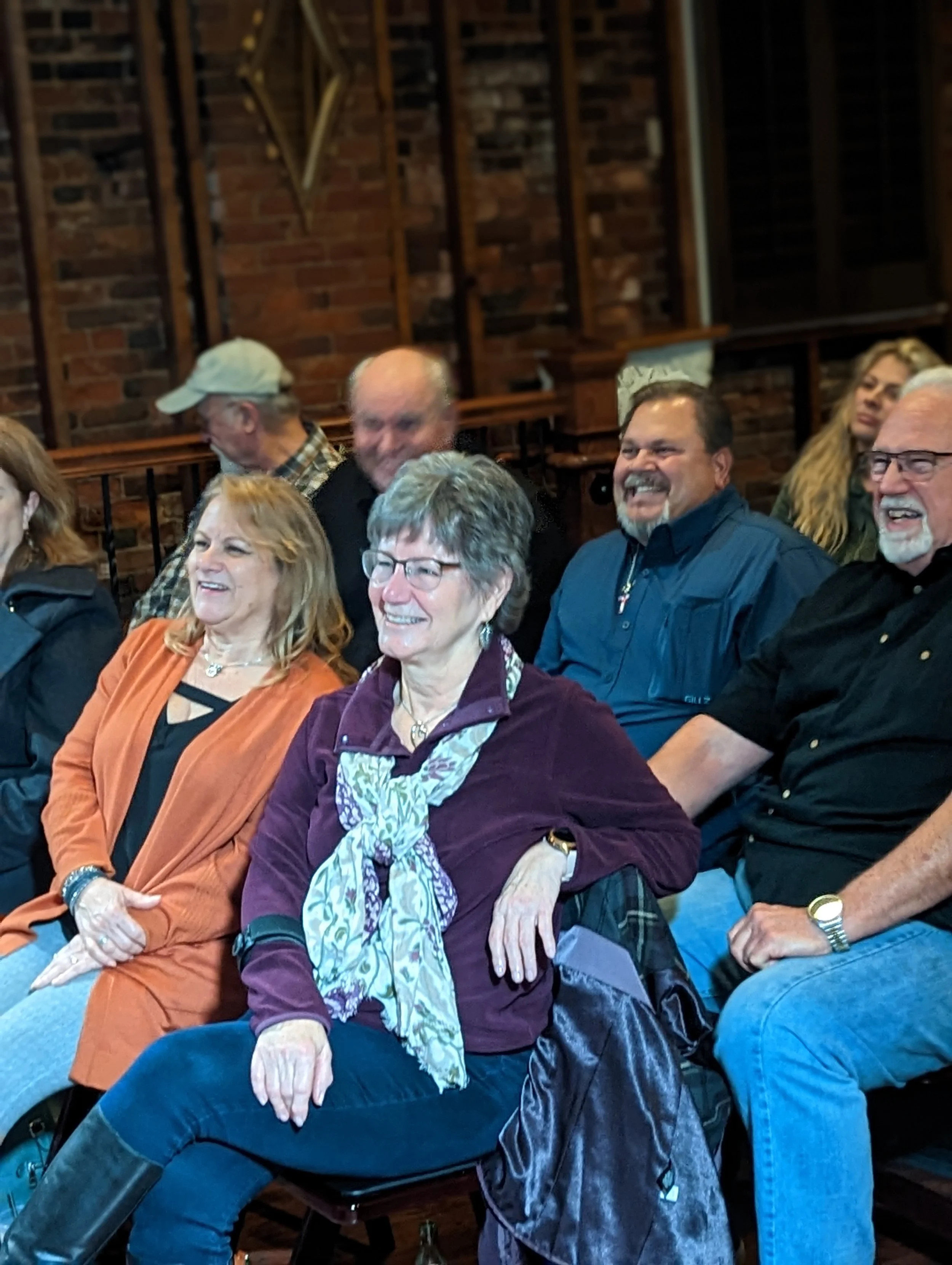 People sitting and laughing in a cozy indoor setting with brick walls and wooden shelves in the background.