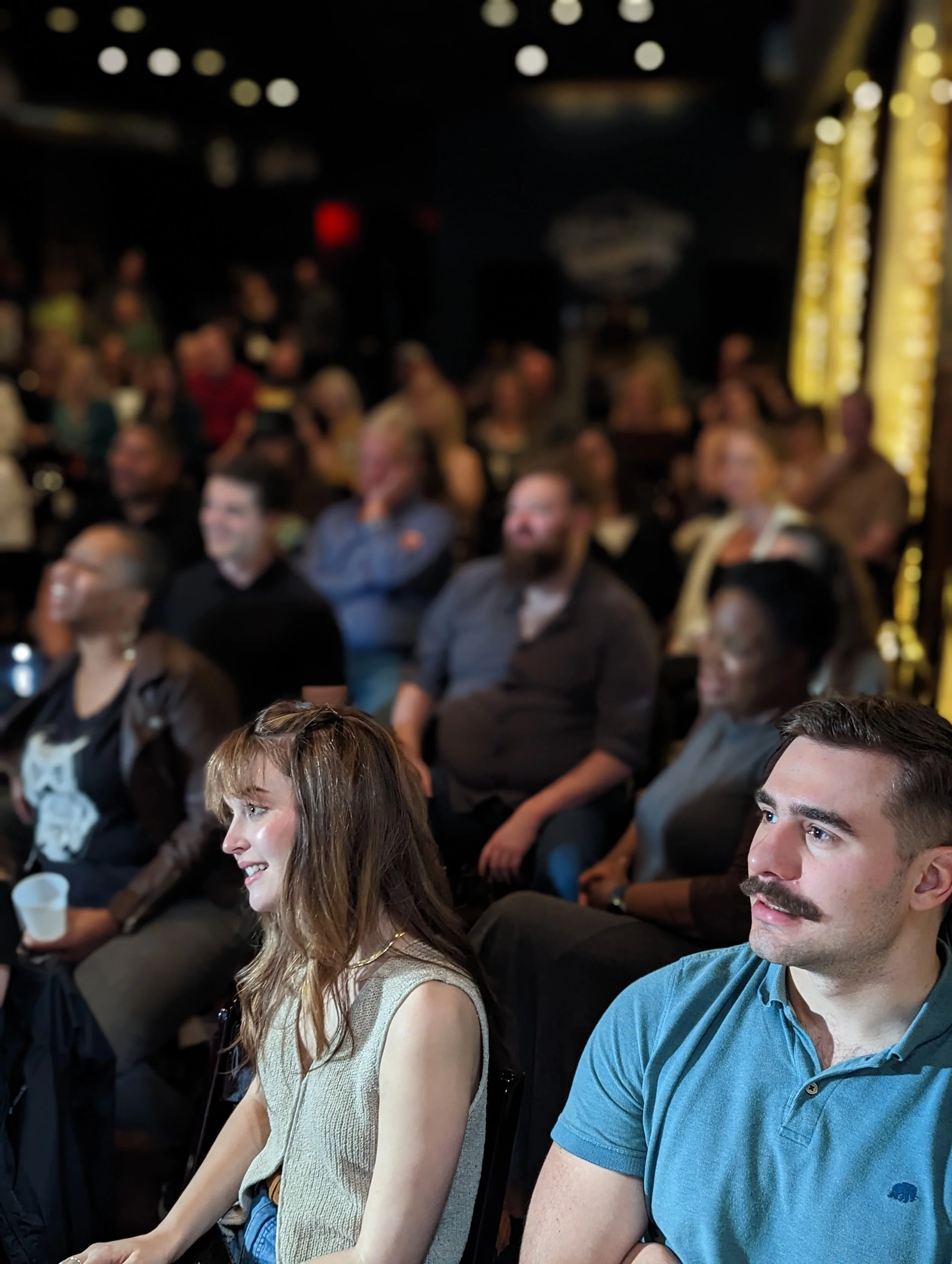 People sitting at tables in a dark room, attending a social event or conference.
