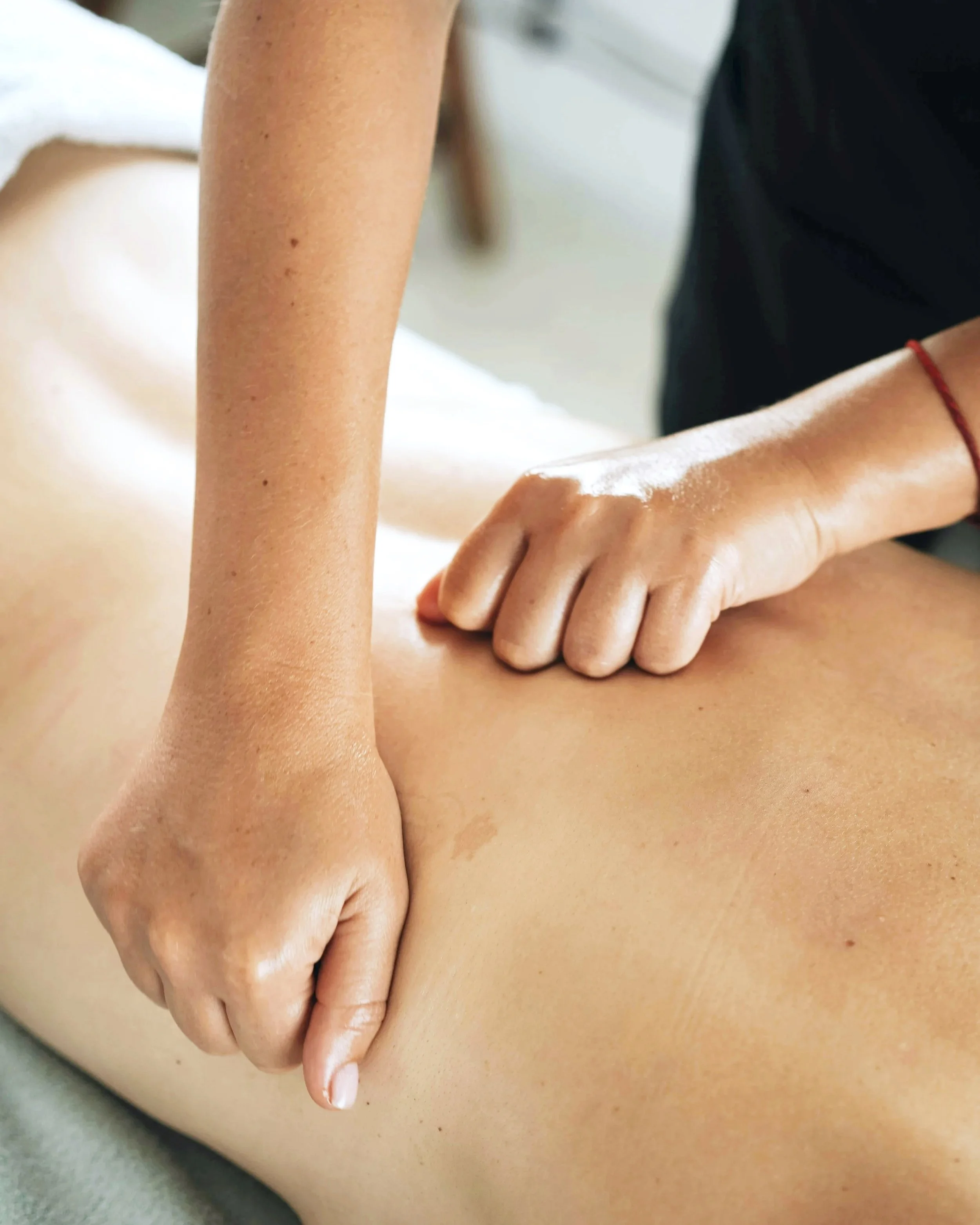 Person receiving massage on lower back with therapist's hands applying pressure.
