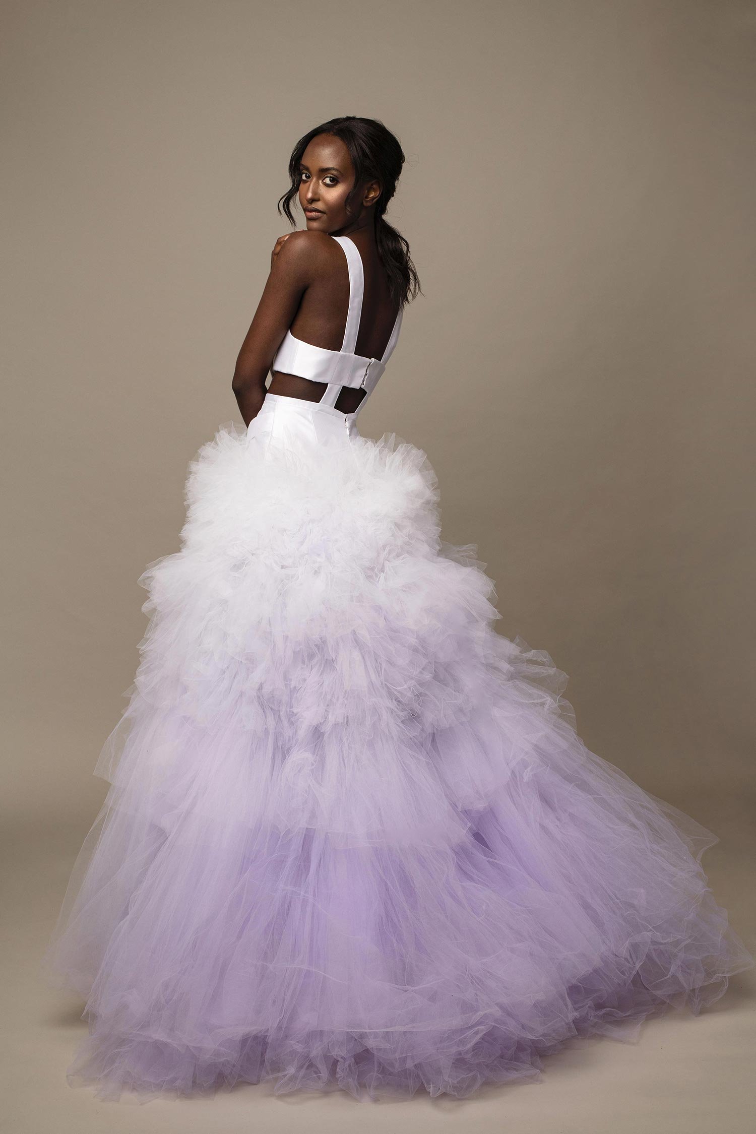 A woman in a white and lavender ruffled gown with a fitted bodice and sheer straps.