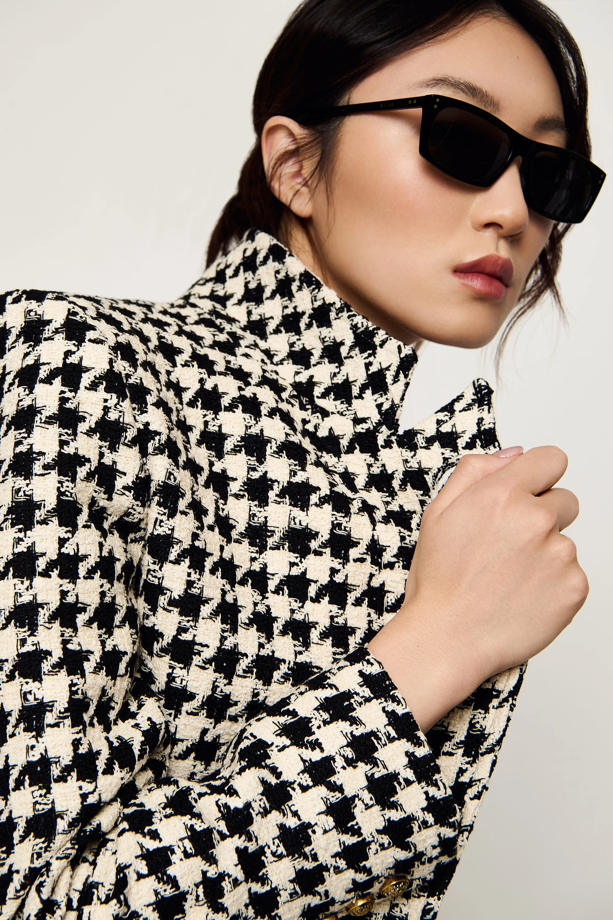 A woman wearing black sunglasses and a black-and-white houndstooth patterned jacket.