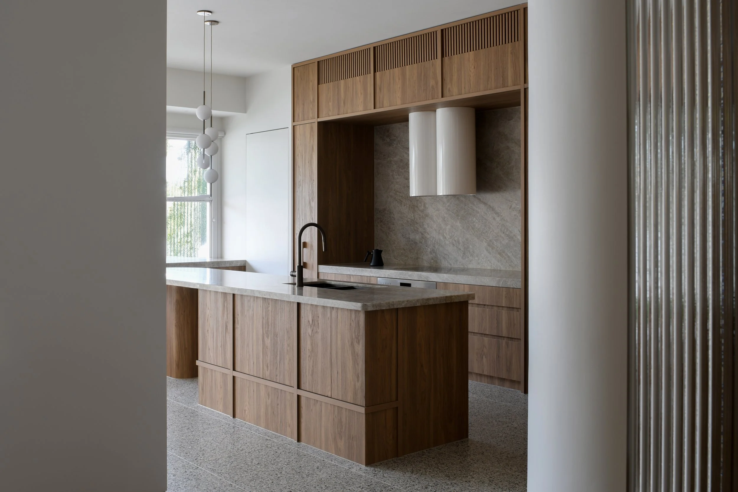 Modern kitchen with wooden cabinets, a marble backsplash, a countertop with a sink, and a black faucet, with a hanging ceiling light near a window.