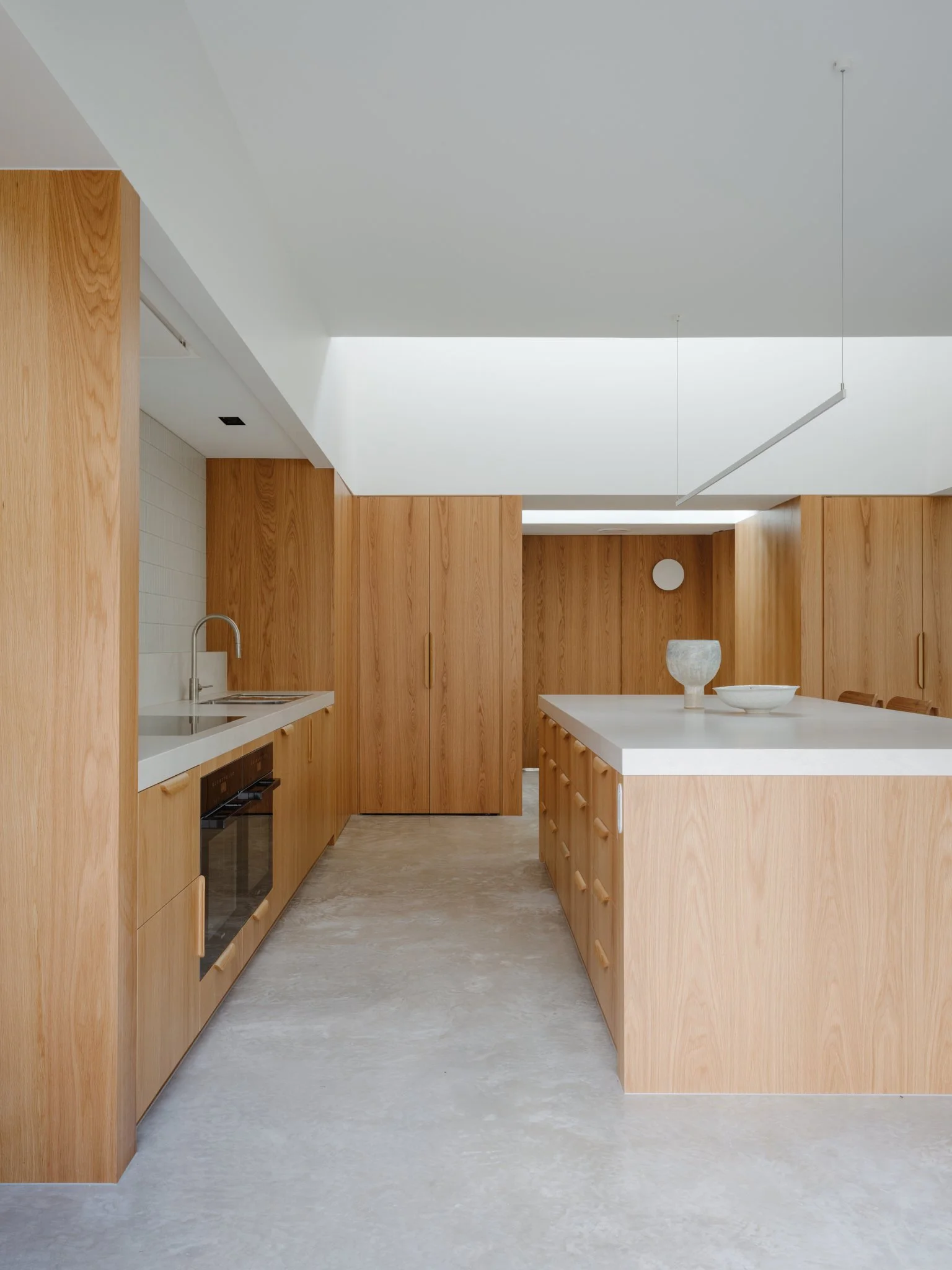 Modern kitchen with wooden cabinets and white countertops, minimalist decor, and a light-colored floor.