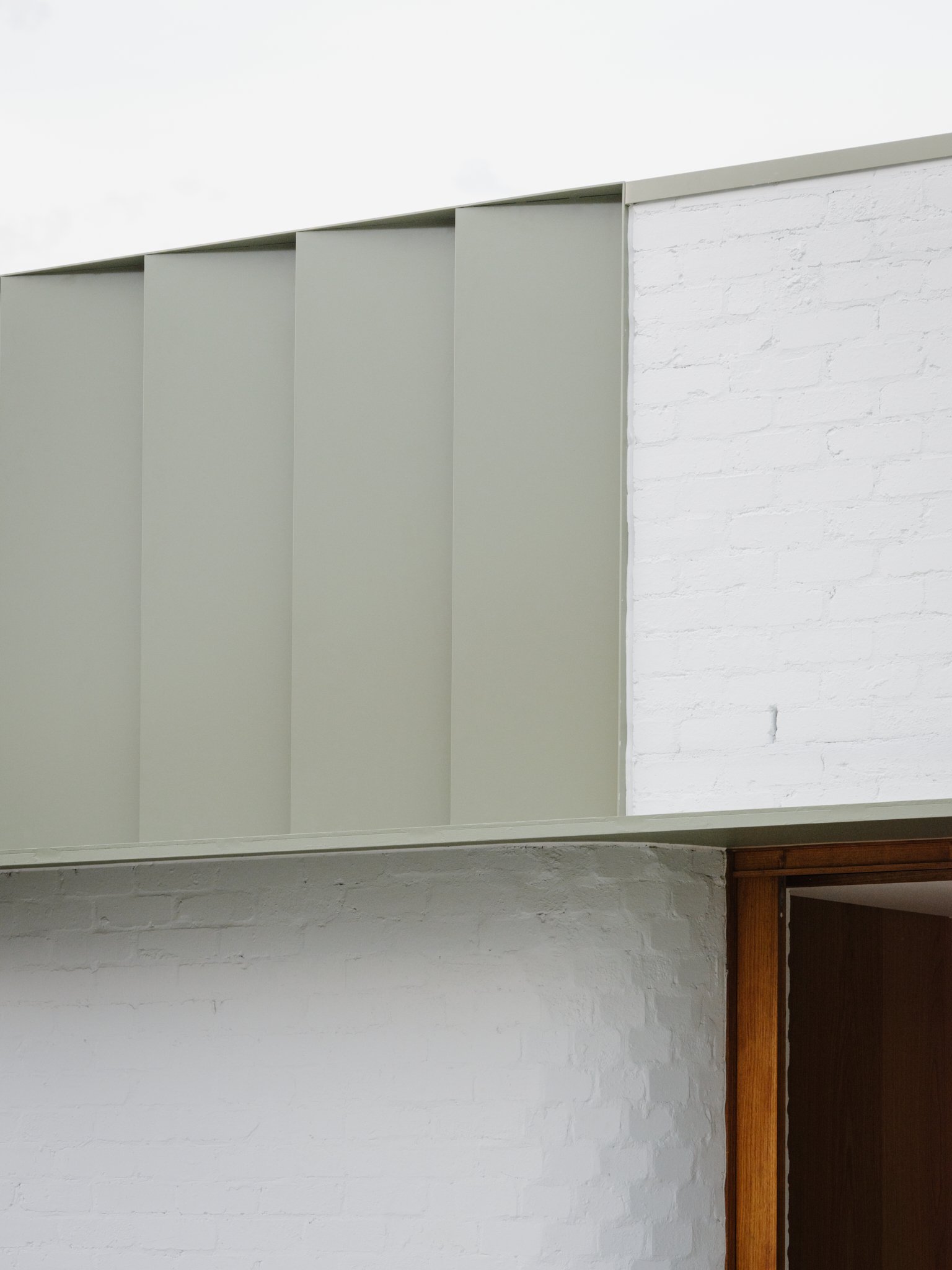 Close-up of a modern, minimalist interior wall with white brick and a separation wall in sage green with vertical panels.