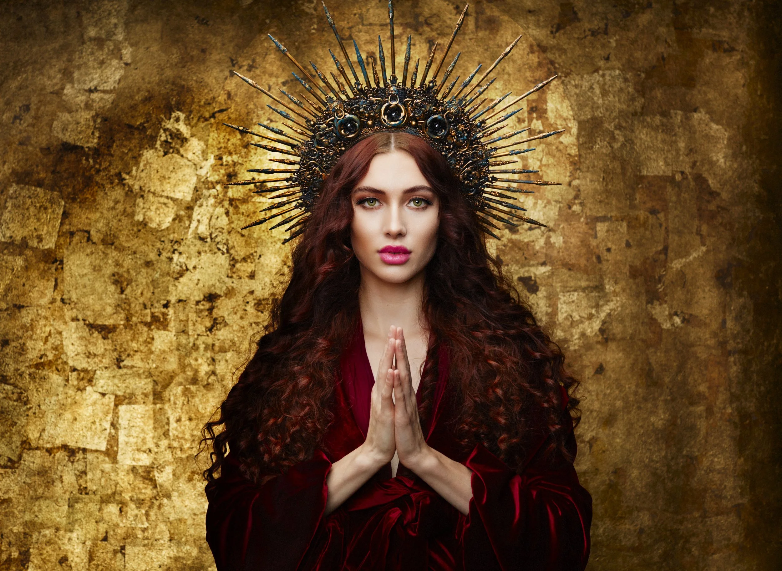 Portrait artistique d’une femme en rouge, les mains jointes, avec une couronne dorée sur fond texturé.
