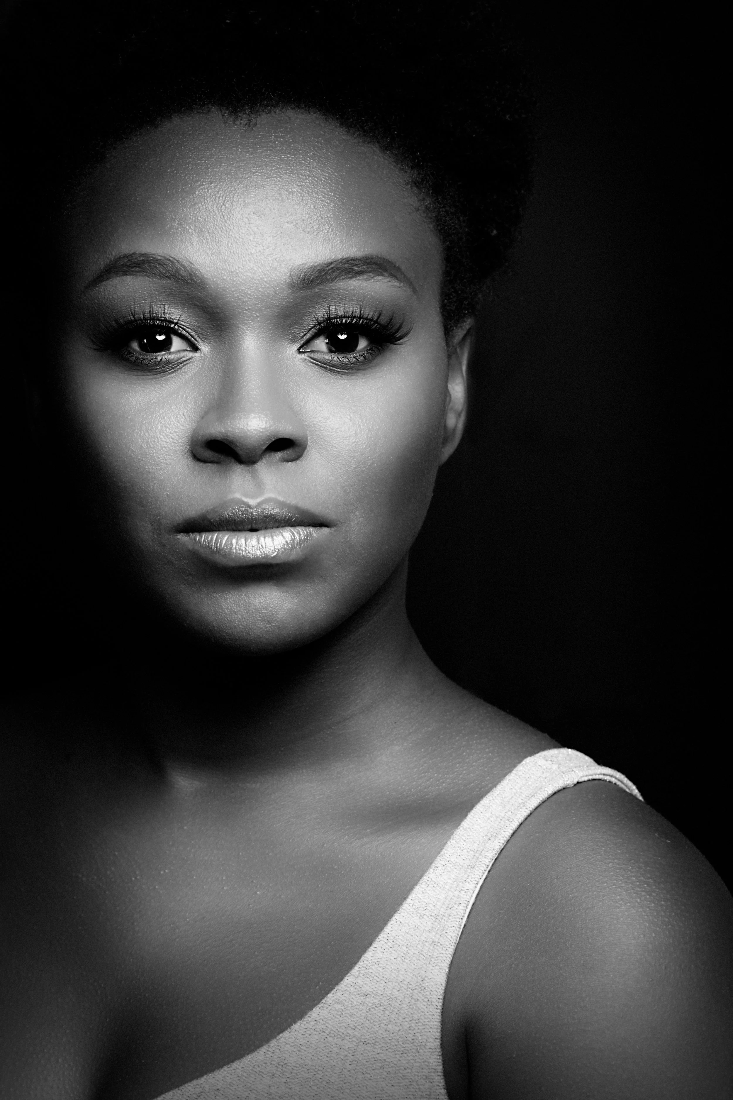 Portrait en noir et blanc d’une femme au regard direct, photographiée sur fond sombre en lumière de studio.