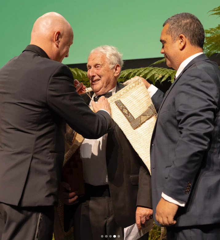 Dr Jim Salinger_2024 NZer of Year with PM_being awarded cloak & trophy.jpg.png