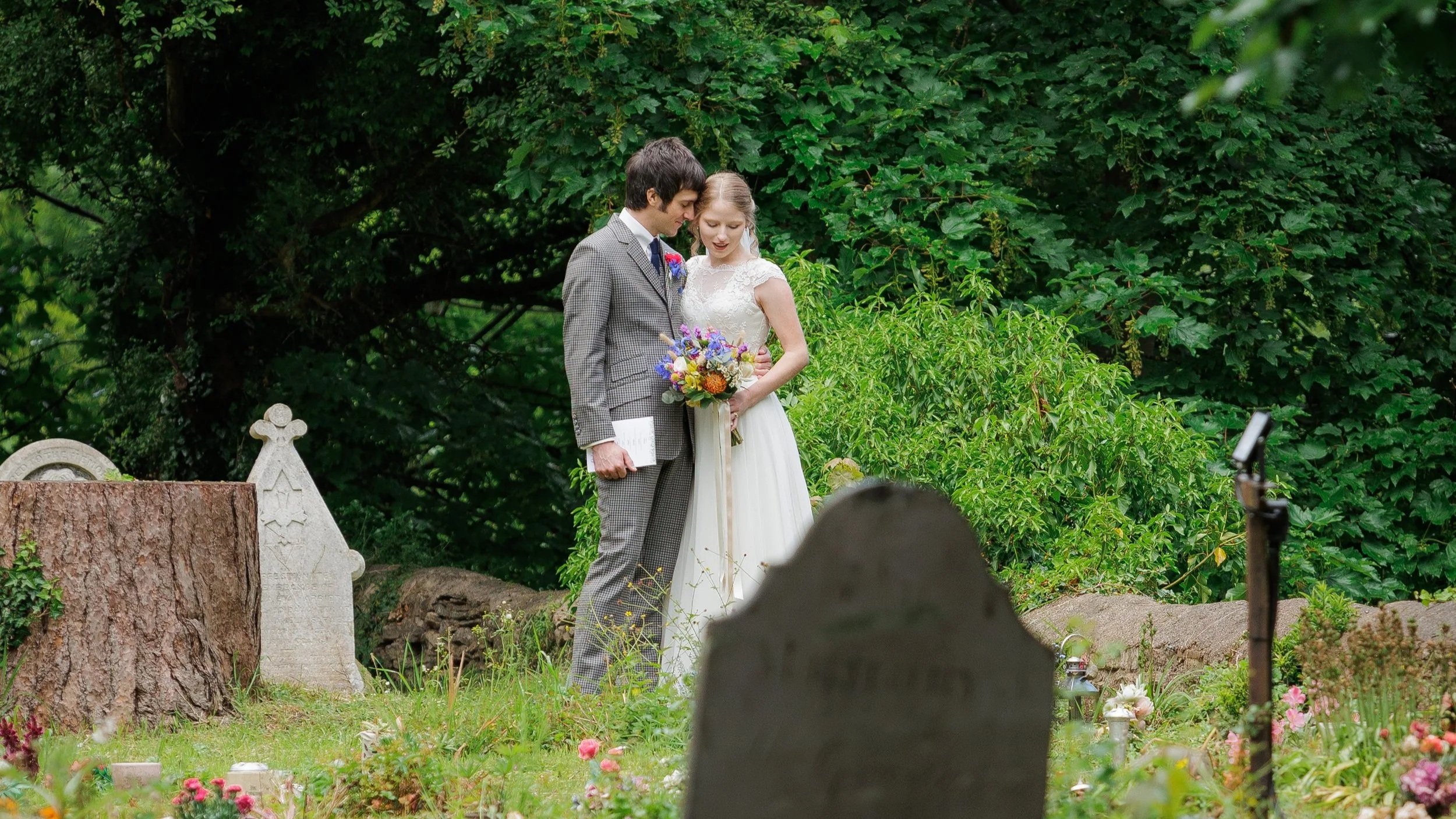 A bride and groom stand in a church yard amongst graves - Planning a wedding without a loved one