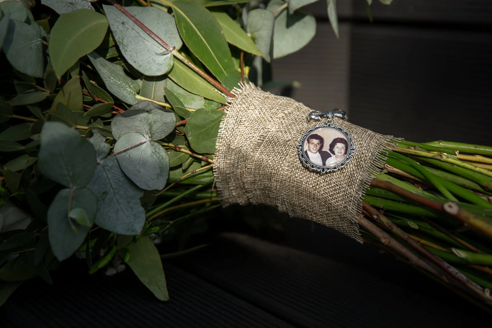 a boquet lies on it's side, hessian cloth rapped round the middle with a charm laying on top. The charm has a vintage hoto of a couple inside. Planning a wedding without a loved one