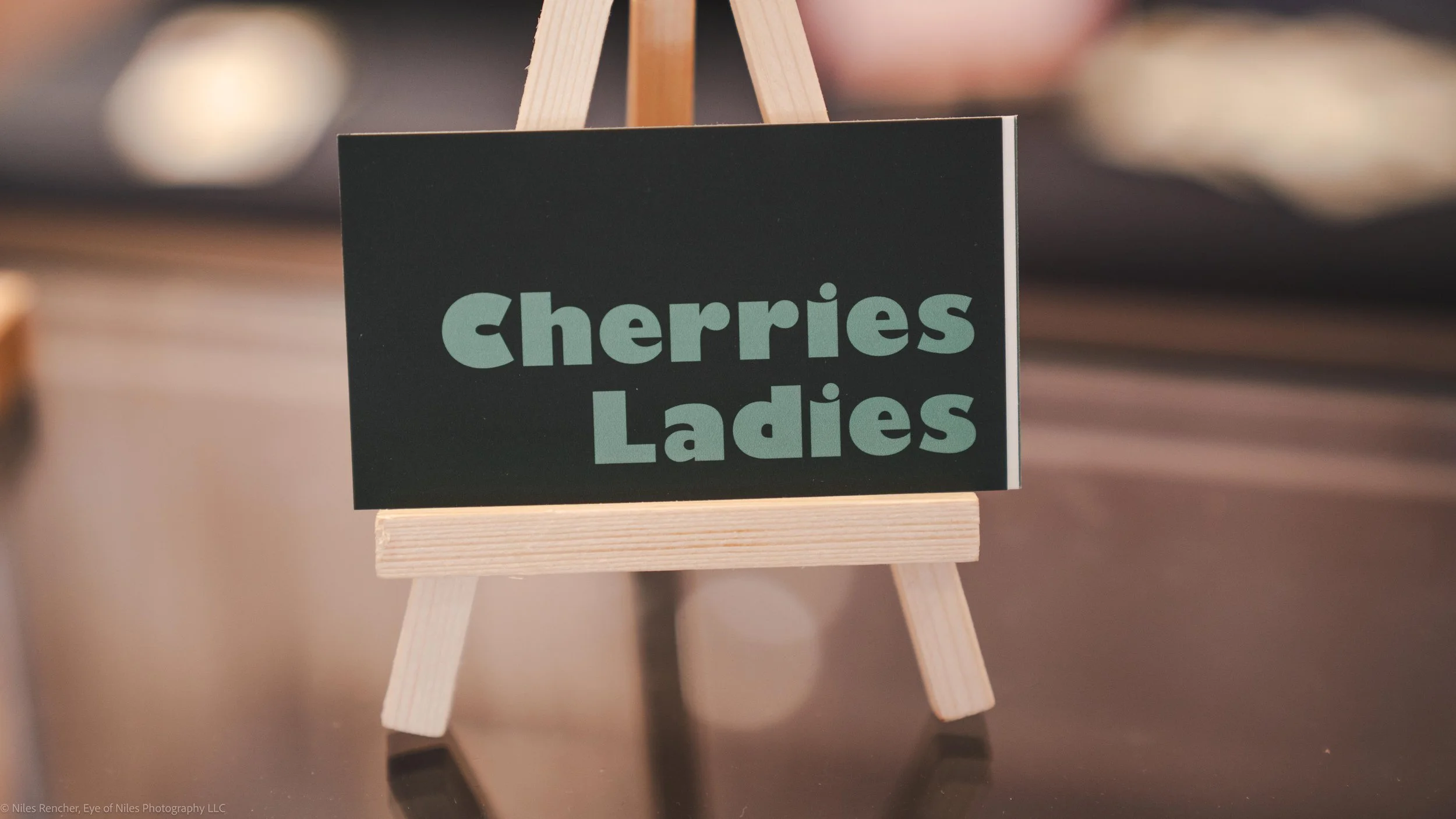 Small business card that reads "Cherries Ladies" on a wooden stand.