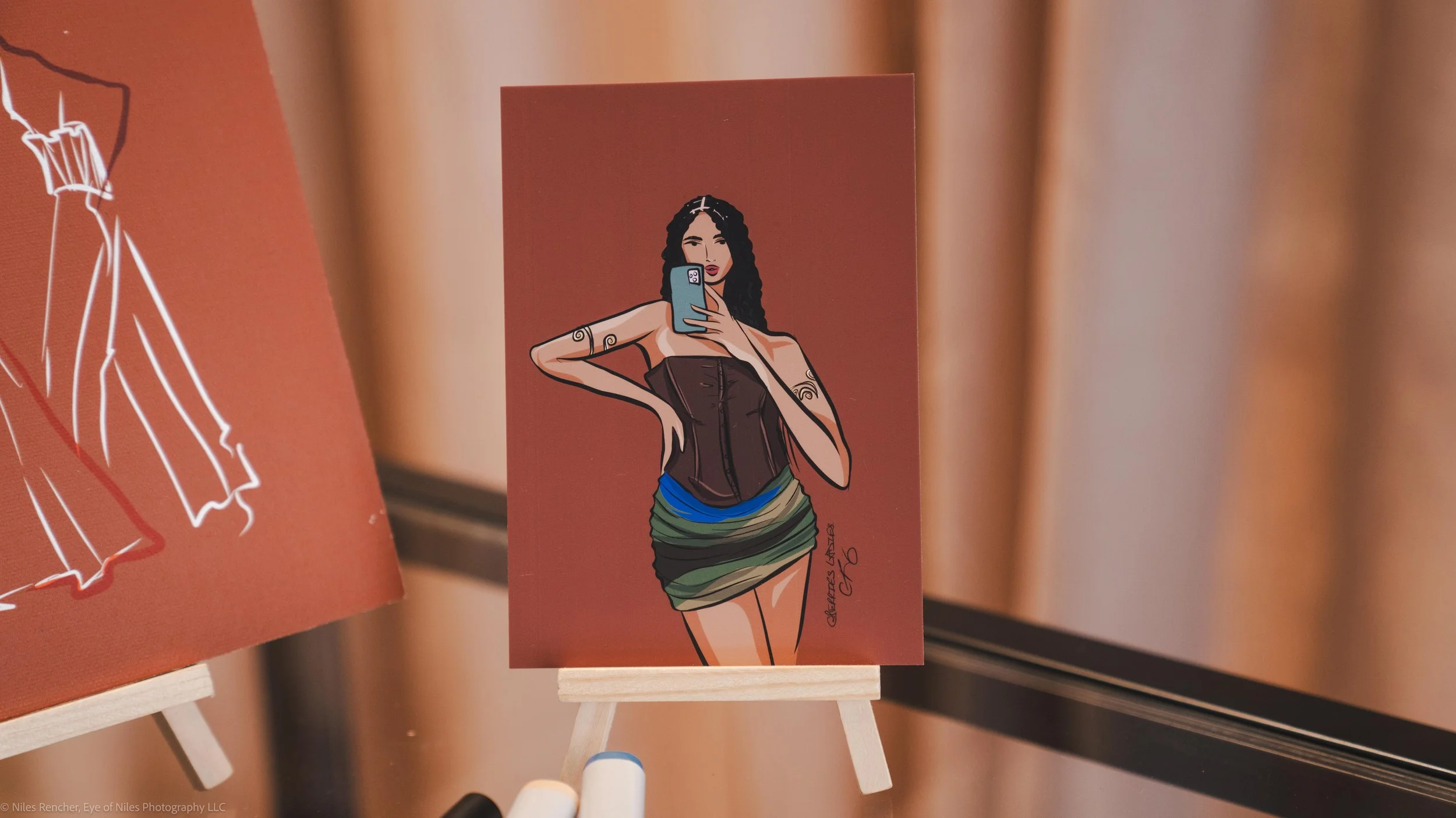 Illustration of a woman with long dark hair taking a selfie with her phone, wearing a strapless brown top and a multicolored mini skirt, with tattoos on her arms, against a plain background. From Cherries Ladies Live Illustration and Eye of Niles
