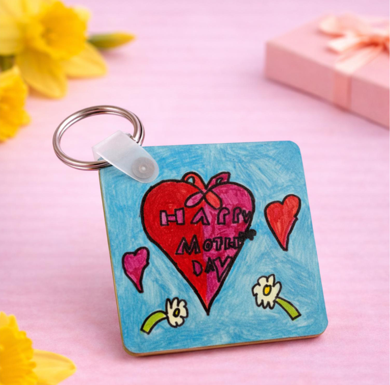 Colorful hand-drawn design on a keyring with hearts, flowers, and the message "Happy Mother's Day" on a pink background, surrounded by yellow flowers and a pink gift box.