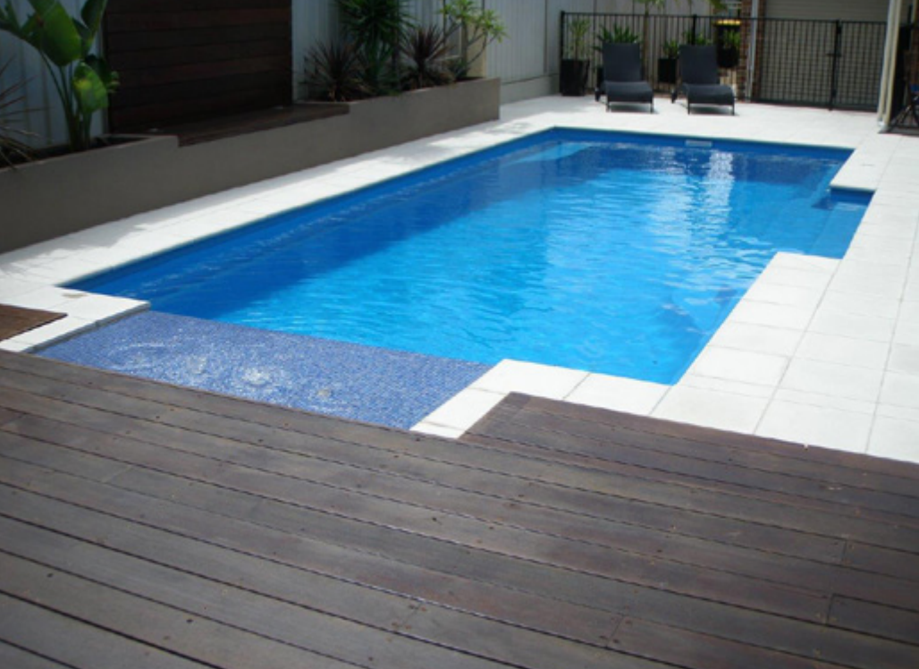 A rectangular swimming pool with blue water, surrounded by white tiled decking.