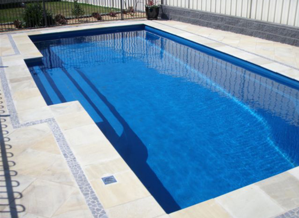 A small rectangular swimming pool with clear blue water, surrounded by white tiles.