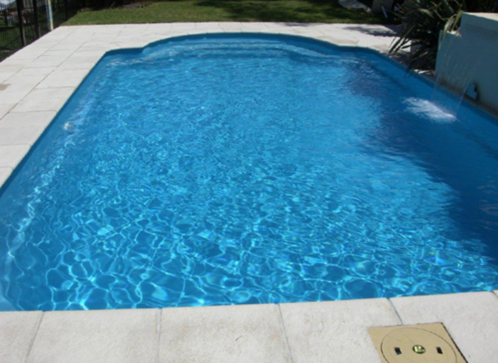 A rectangular pool filled with clear blue water, surrounded by a white tiled deck.
