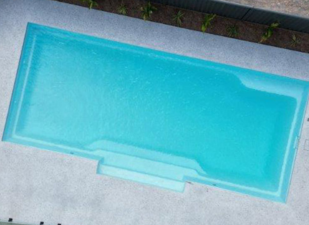 Rectangular swimming pool with clear blue water surrounded by white tiles