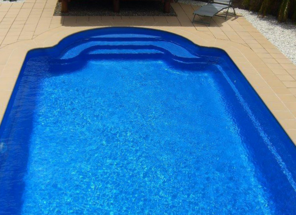 A rectangular swimming pool filled with clear blue water, surrounded by a white tiled deck.