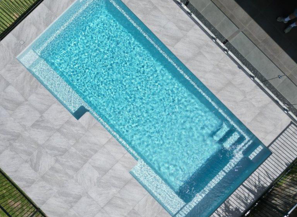Empty rectangular swimming pool with blue water and light-colored tile surrounding it.
