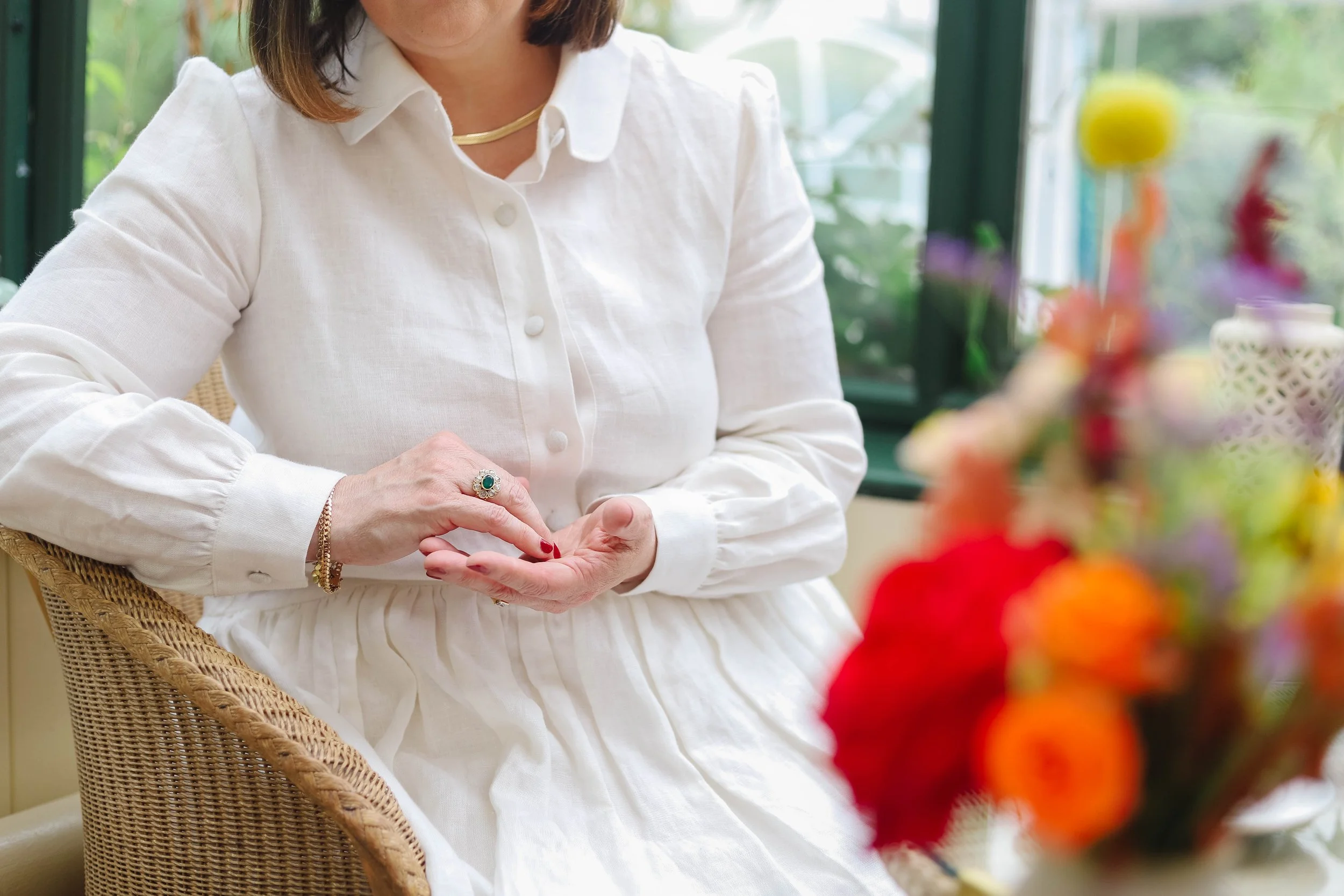 Lucy O'Reilly from Designs For Growth in a white blouse sitting indoors, and a blurred colourful bouquet in the foreground.