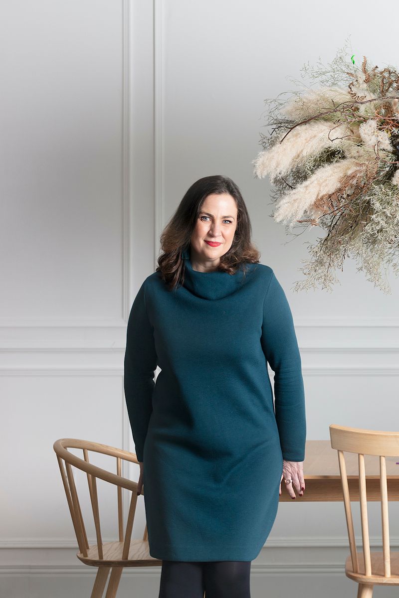 Lucy  O'Reilly of Design For Growth in a teal dress leaning against a meeting table