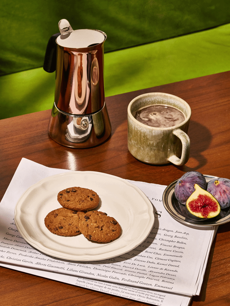 Tasse de chocolat chaud, plateau avec trois cookies, cru et cuit, et des figues fraîches sur une table en bois.