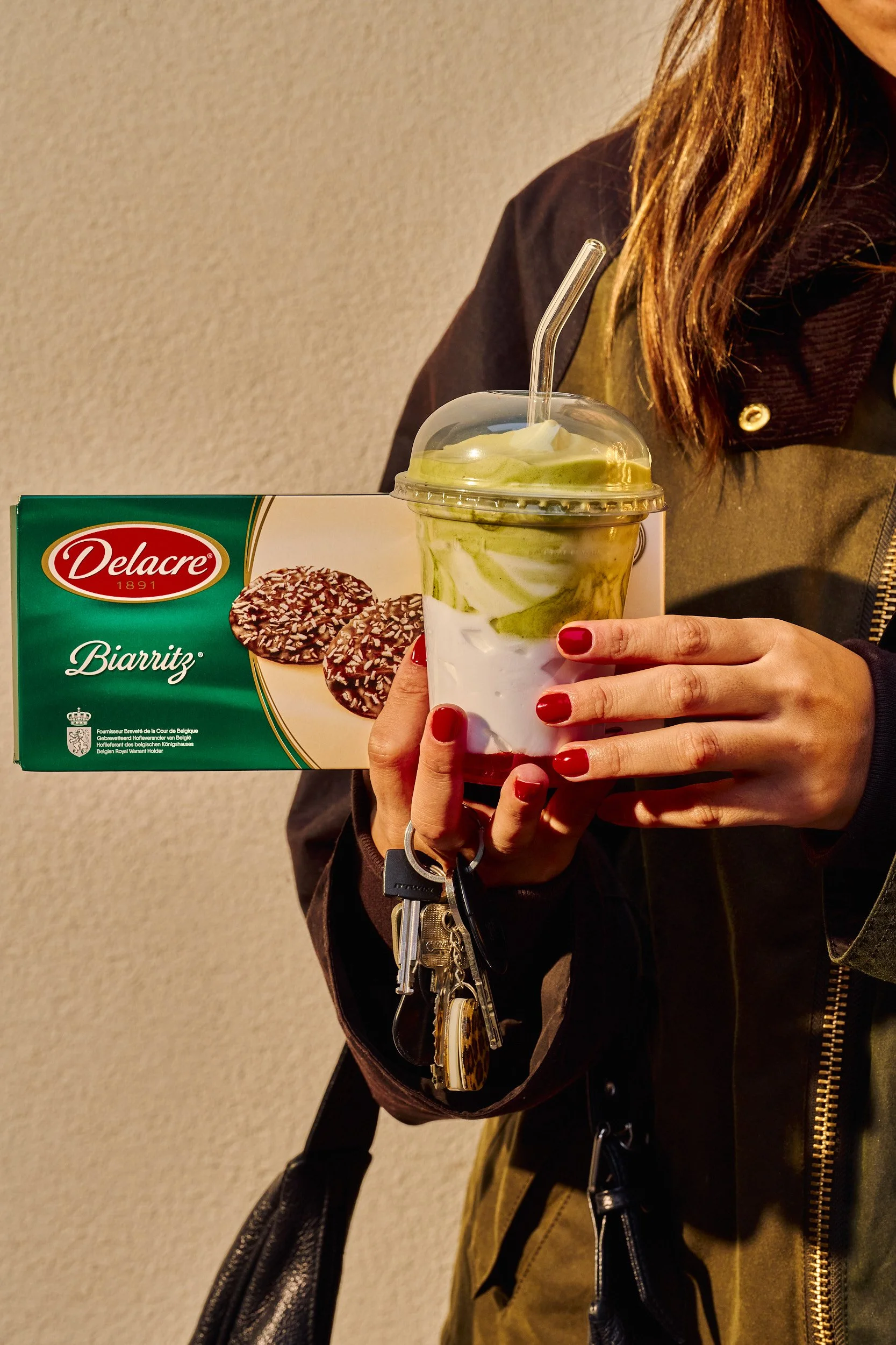 Une personne tient une boîte de biscuits Delacre Biarritz et un smoothie avec des tranches de kiwi à l'intérieur.