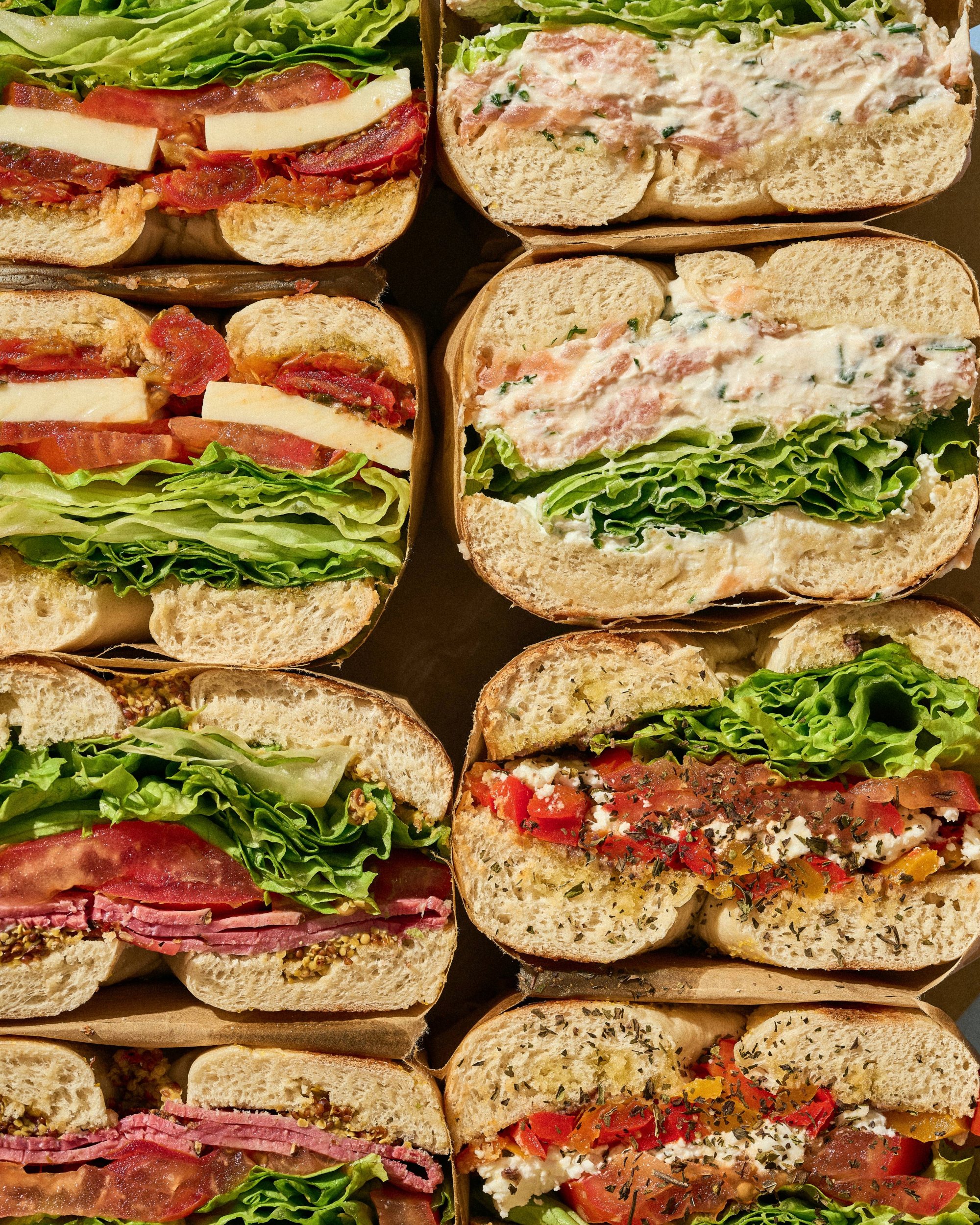 Divers sandwiches garnis de laitue, viande, fromage et tomates présentés en gros plan.
