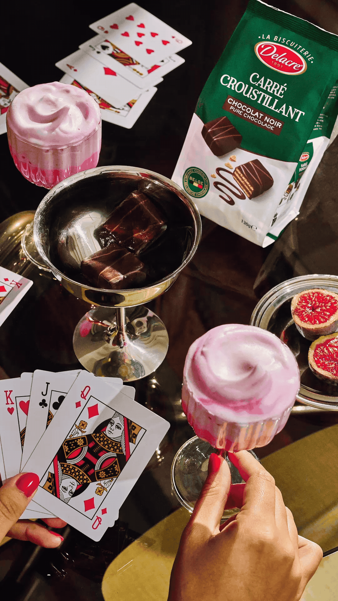 Un jeu de cartes, deux cocktails avec des glaçons en forme de carrés, des biscuits au chocolat et des figues coupées.