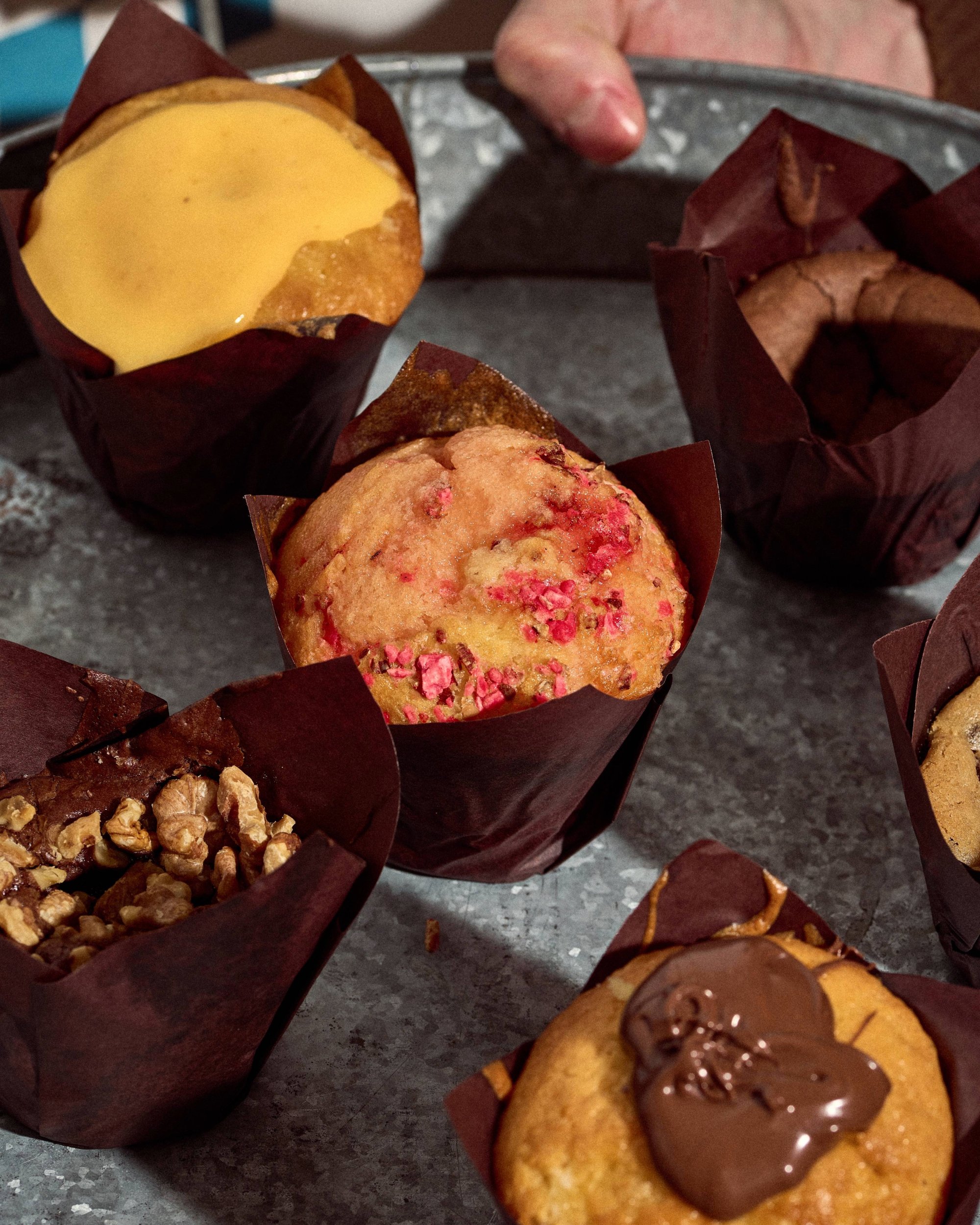 Plateau de muffins variés avec glaçage et noix, photographiés sur une table.